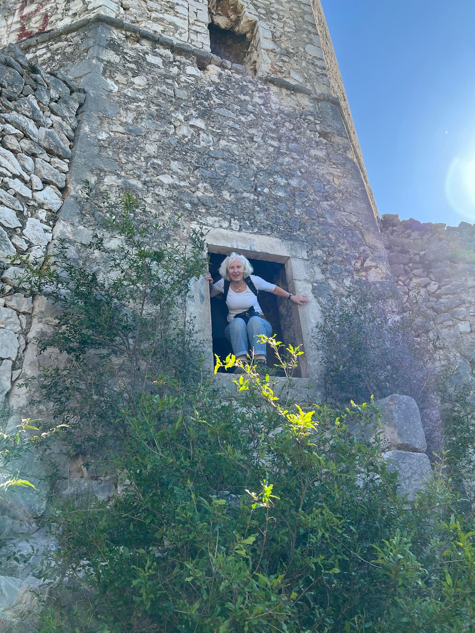 Po?itelj Fortress stone window with a woman leaning out, shrubs below and bright sky, Po?itelj, Bosnia and Herzegovina.