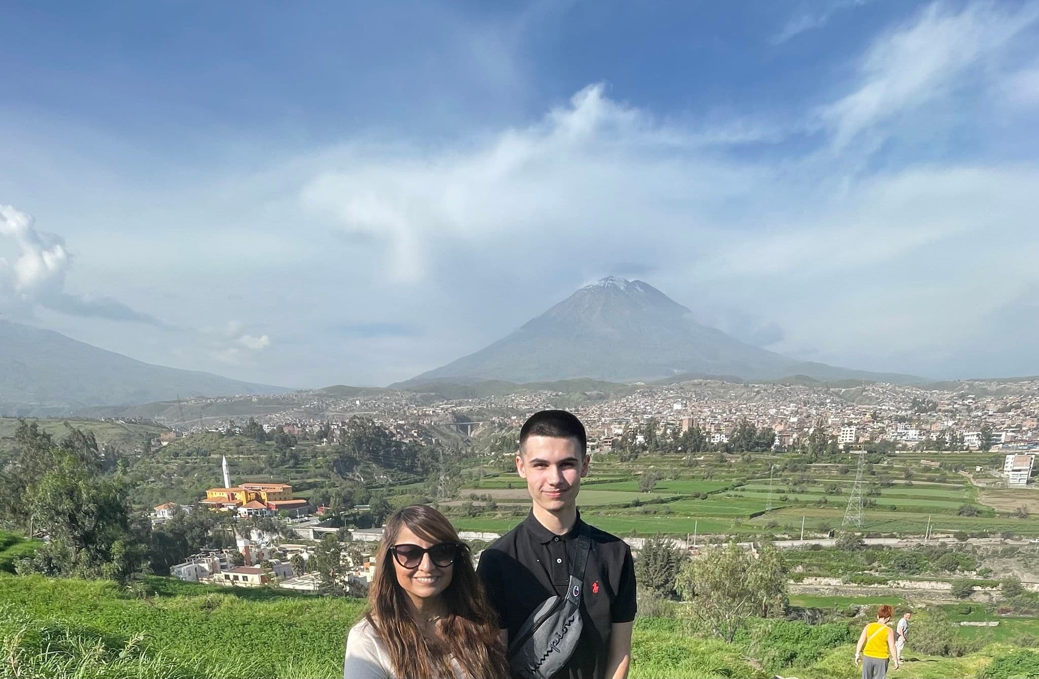 El Misti volcano rising above Arequipa, Peru, with two people posing on a grassy hill in the foreground.
