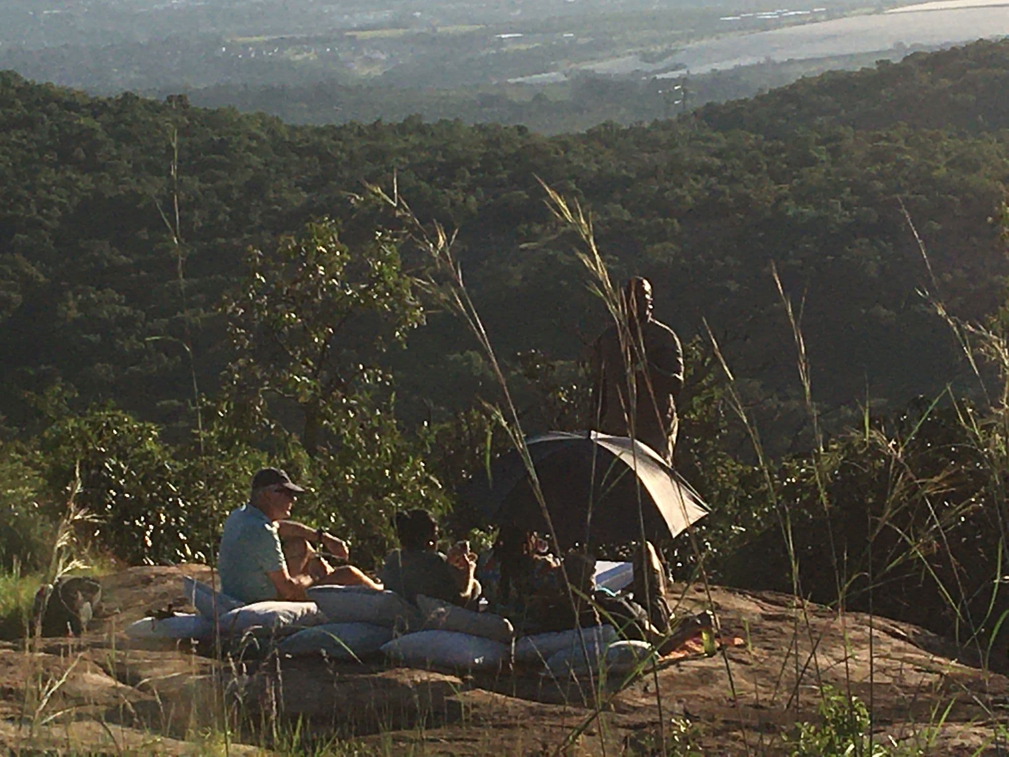 Group of travelers enjoying sundowners on a rocky cliff near Kruger National Park, South Africa, overlooking a forested valley.