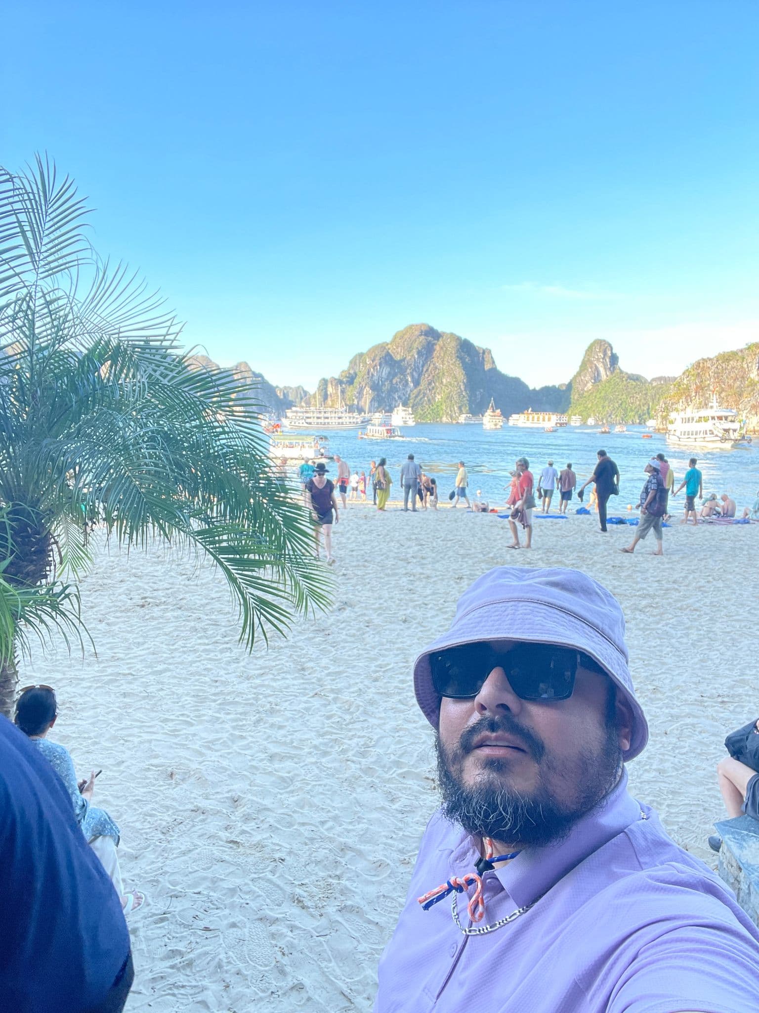 Limestone karsts of Ha Long Bay with tourists on a sandy beach and a person taking a selfie, Ha Long Bay, Vietnam
