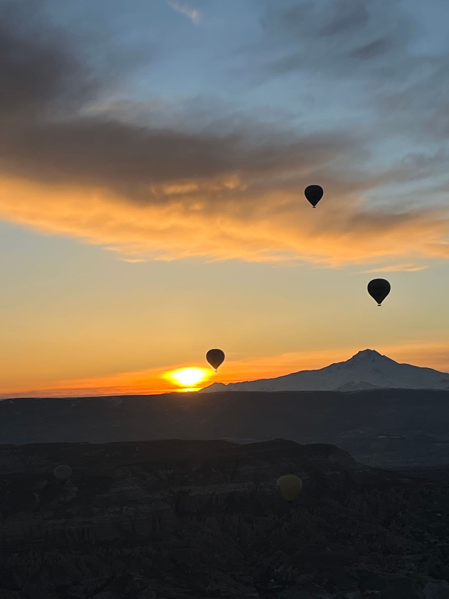 Hot air balloons floating above a sunrise with Mount Erciyes and Cappadocia rock valleys, Turkey.