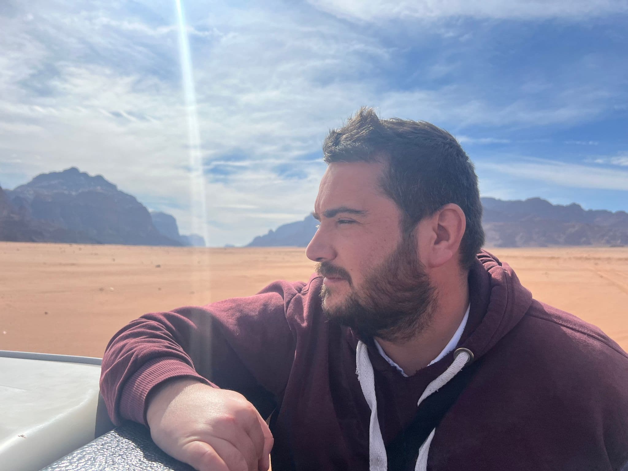 Wadi Rum desert with a man leaning on a vehicle looking toward sandstone mountains, Jordan