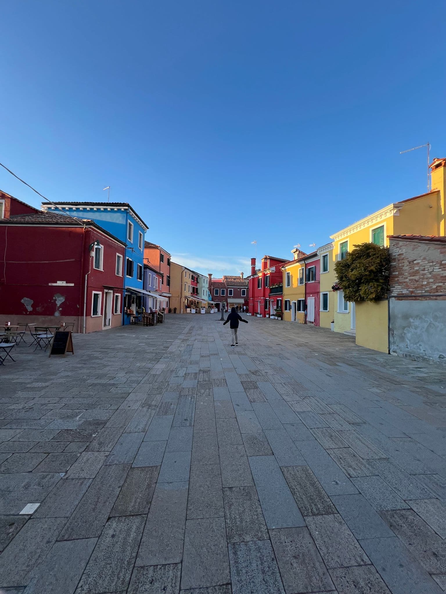 Burano's colorful houses lining a paved square with a person walking toward the center, Burano, Venice, Italy