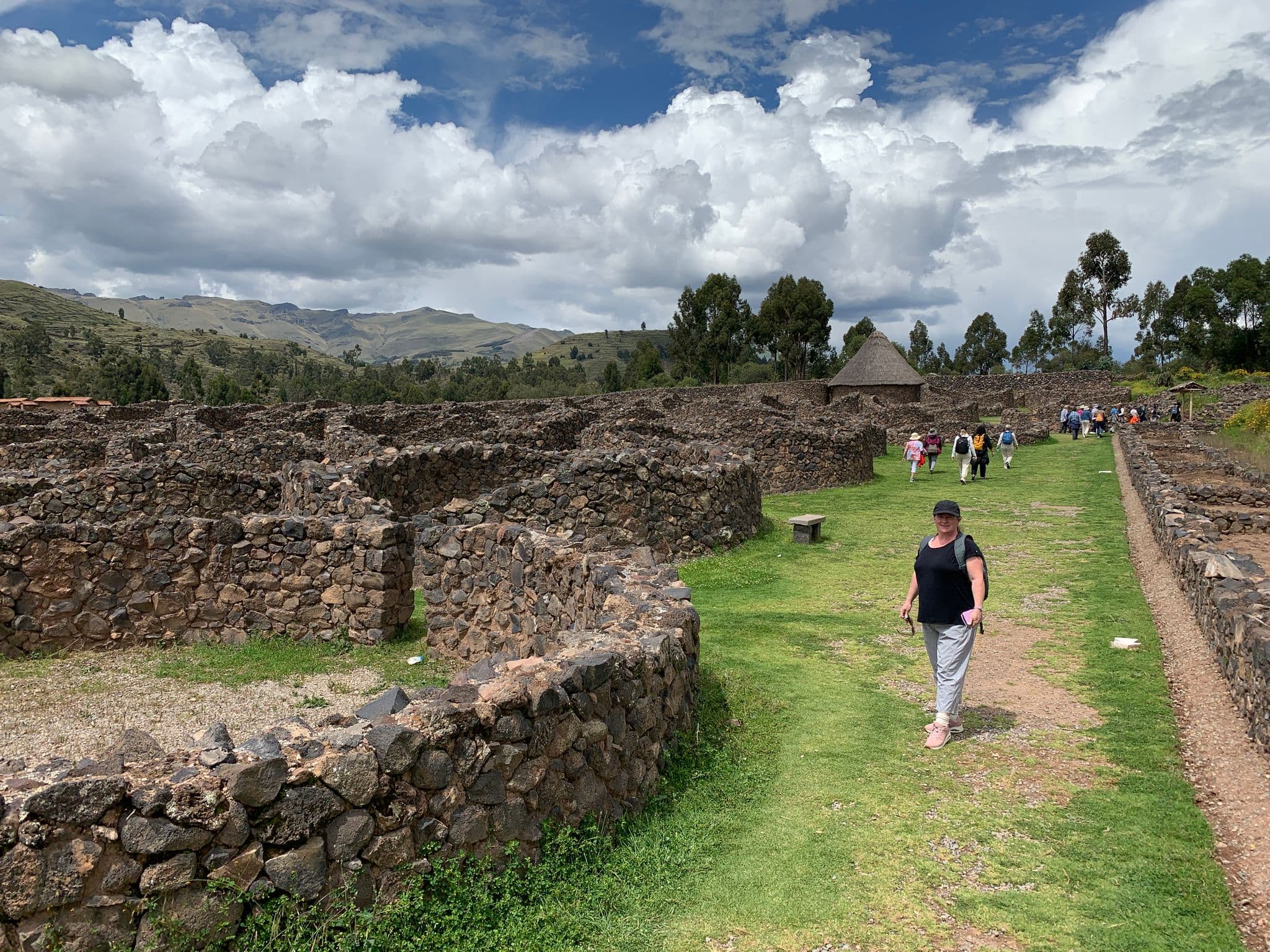Inca stone ruins with visitors walking a grassy path near Cusco, Peru.