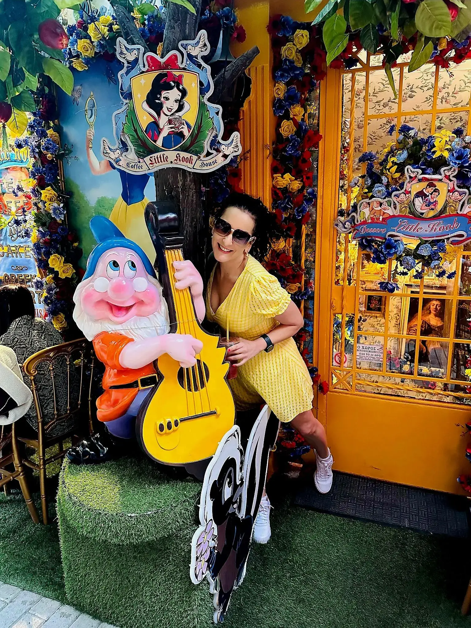 Gnome statue playing a yellow guitar with a woman in a yellow dress posing at Little Kook, Athens, Greece.