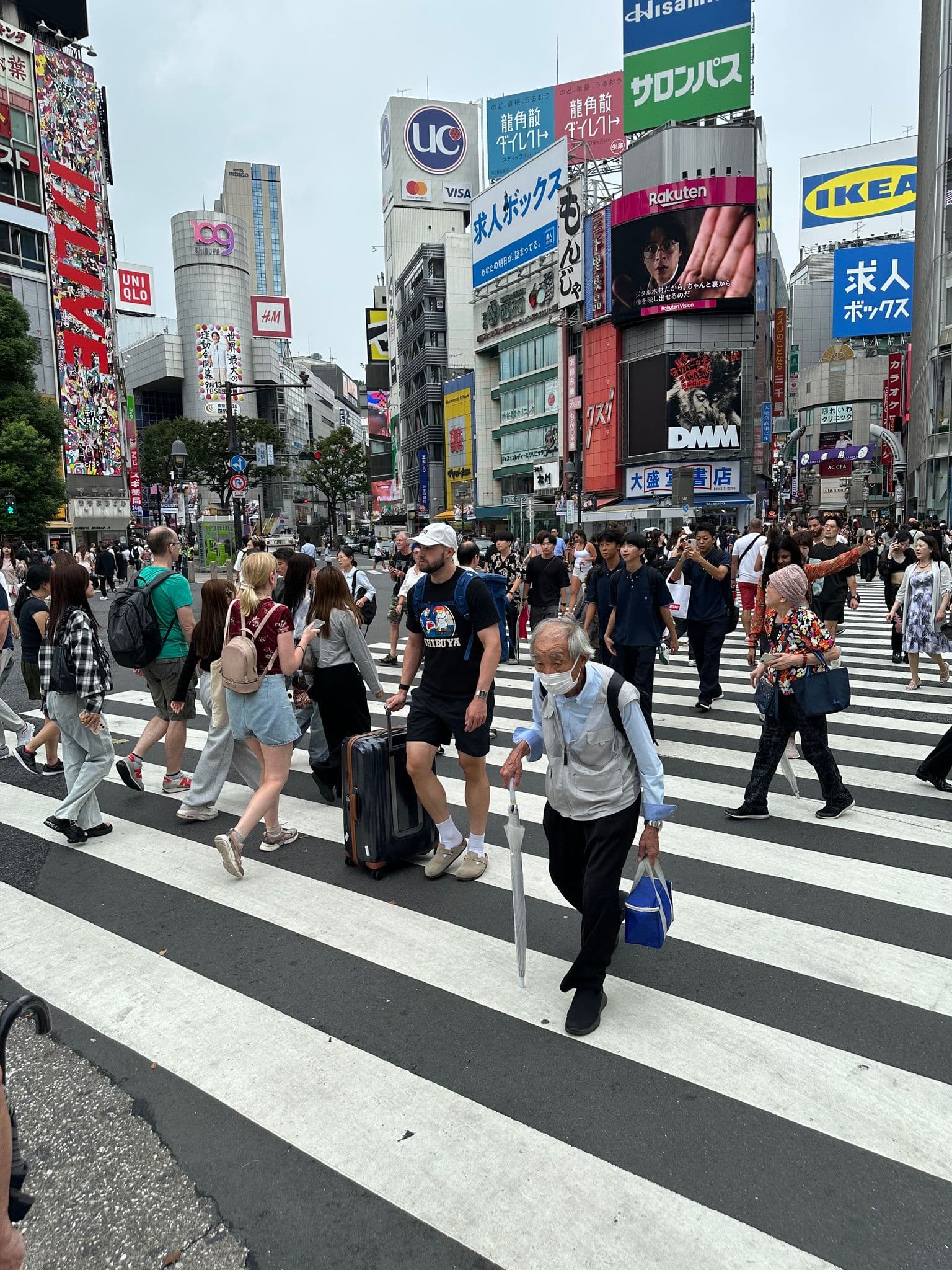 Shibuya Crossing in Tokyo, Japan with crowds of people crossing the striped scramble intersection in front of shopping towers.