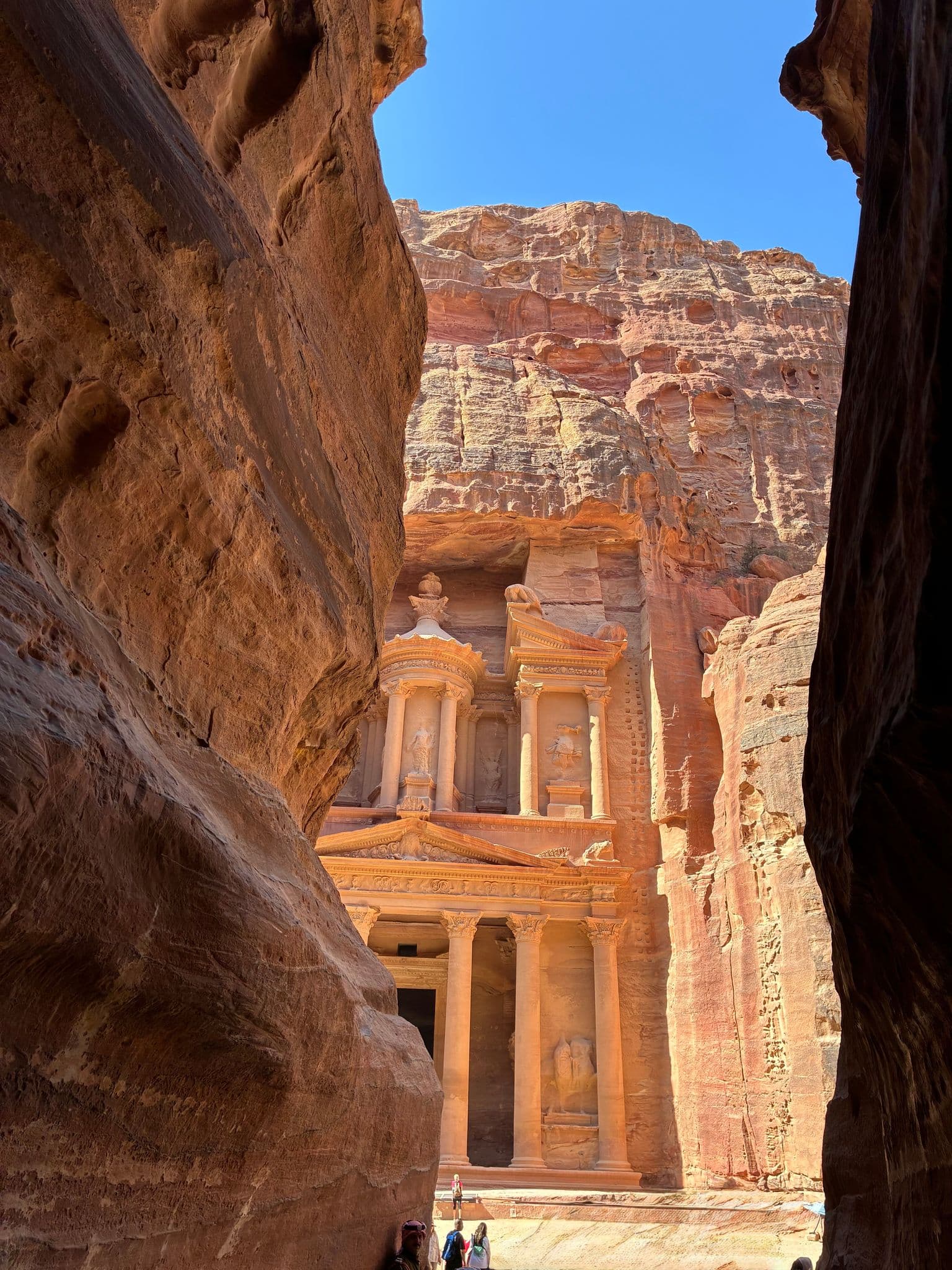 The Treasury at Petra framed by narrow sandstone canyon walls with tourists standing at the entrance, Petra, Jordan.
