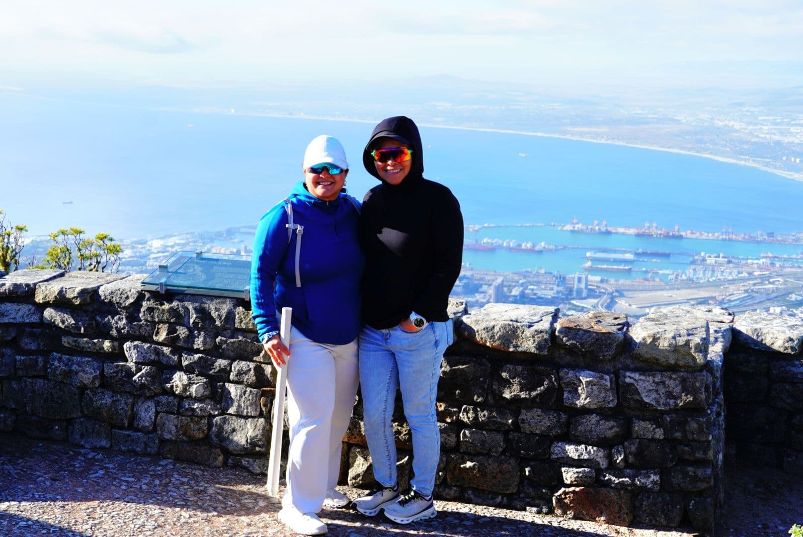View from Table Mountain over Cape Town and Table Bay with two travelers posing by a stone lookout wall