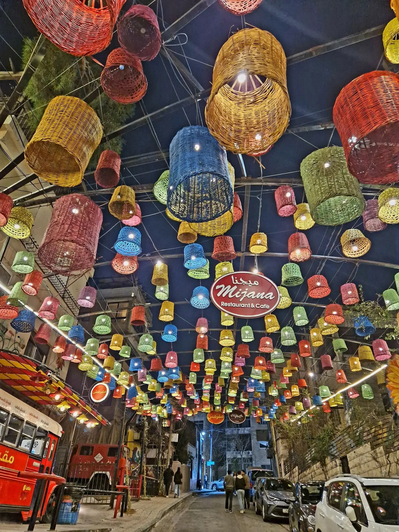 Colorful woven lanterns hung over Rainbow Street in Amman, Jordan, with people walking beneath the lit canopy.