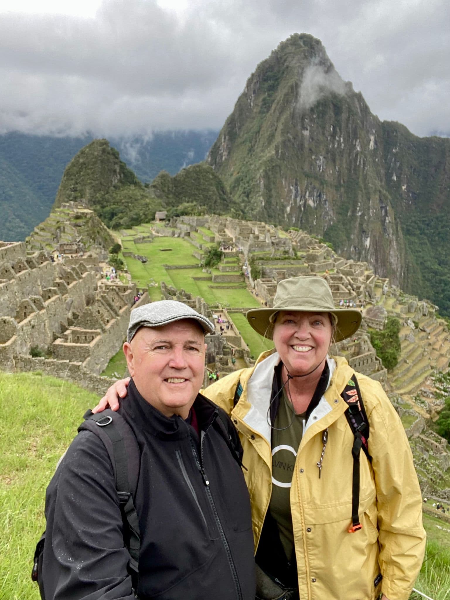 Machu Picchu ruins with Huayna Picchu behind and two travelers posing in the foreground on a trip to Cusco, Peru.