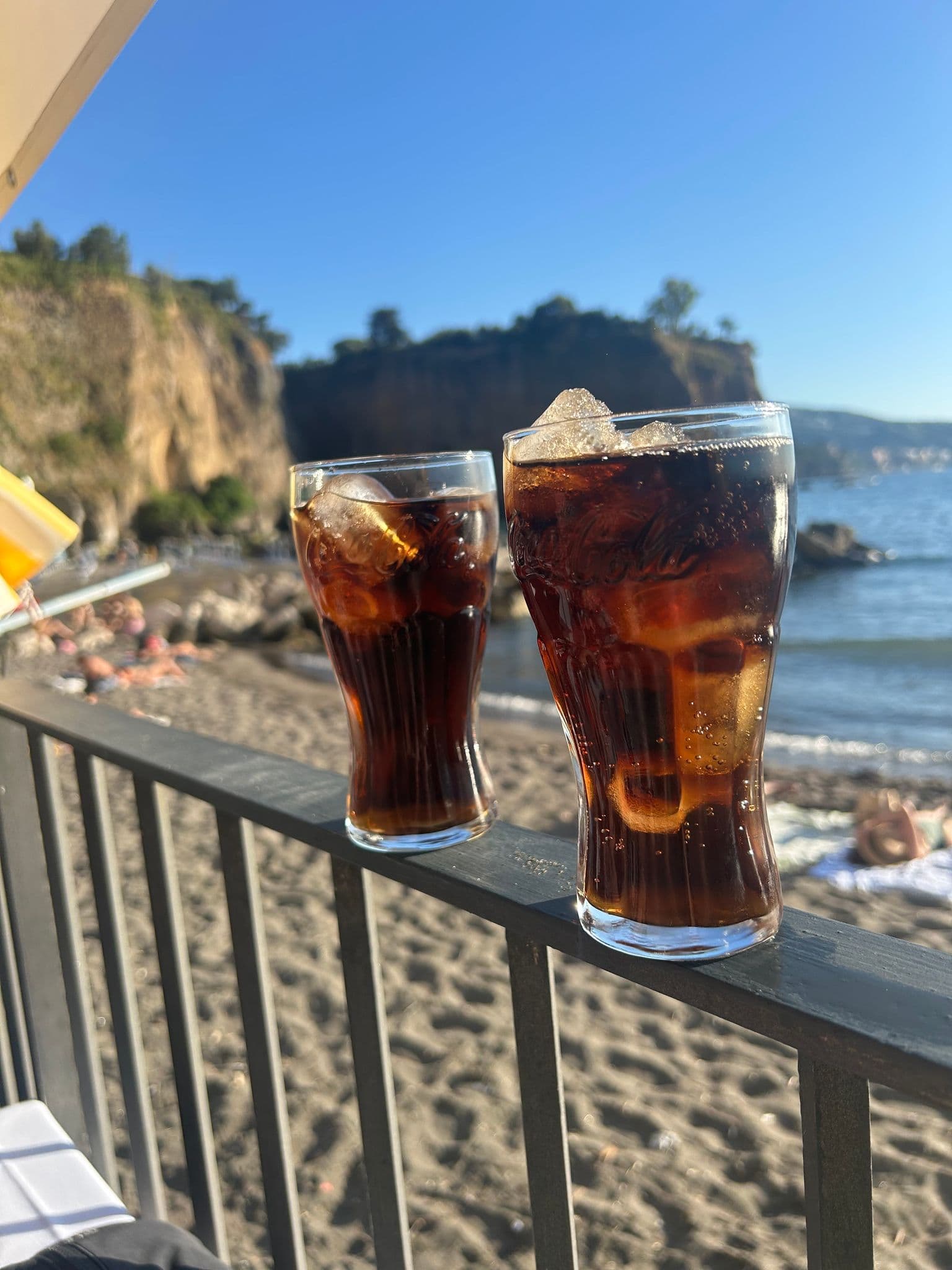 Two glasses of Diet Coke on a railing overlooking the beach and cliffs of Marina Grande, Sorrento, Italy.