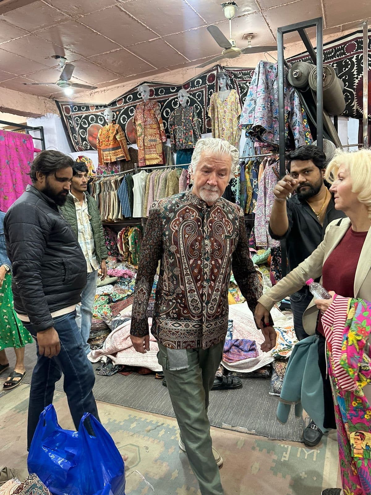 Man wearing a patterned jacket being guided through a crowded textile emporium in Jodhpur, India.