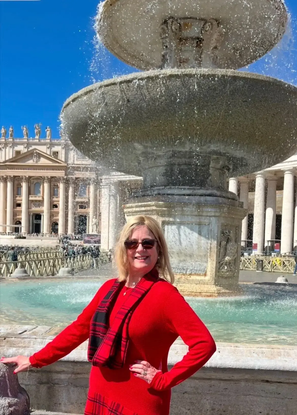 St. Peter's Square fountain with St. Peter's Basilica in the background and a woman posing by the pool in Rome, Italy.