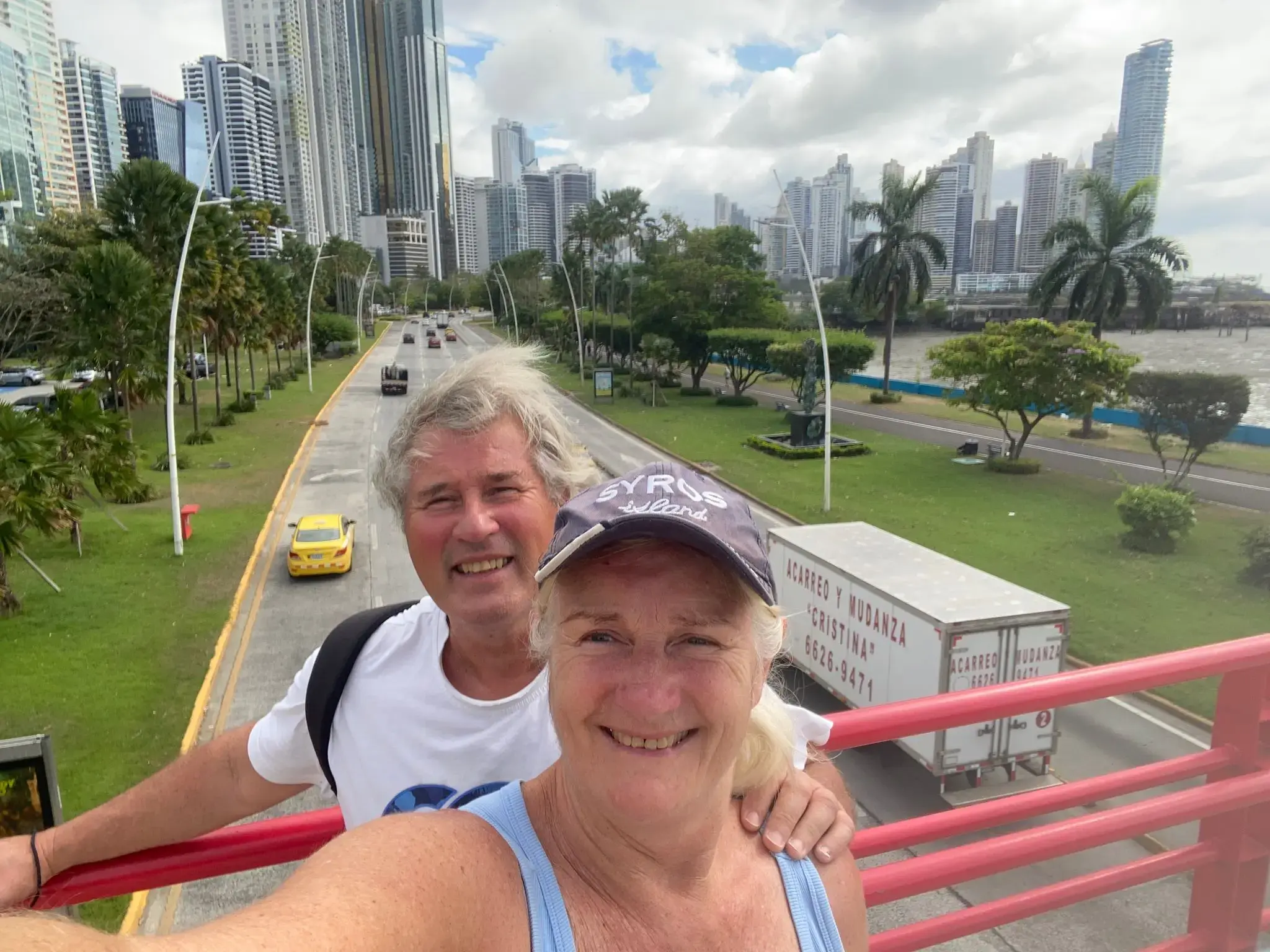 Panama City skyline with two travelers taking a selfie on a pedestrian bridge above a motorway, Panama City, Panama.