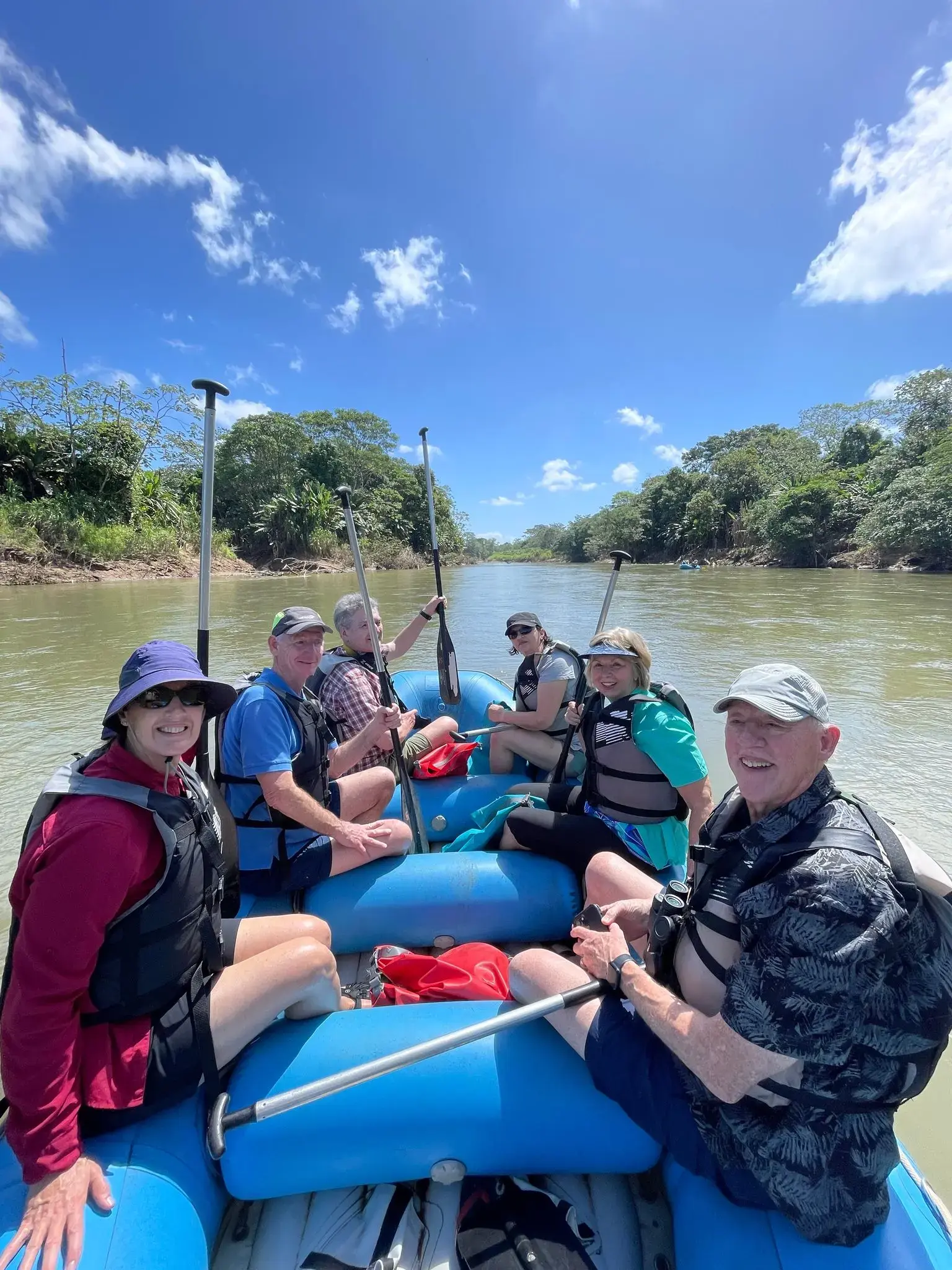 Blue inflatable raft with six people paddling on a river surrounded by tropical forest, Costa Rica.