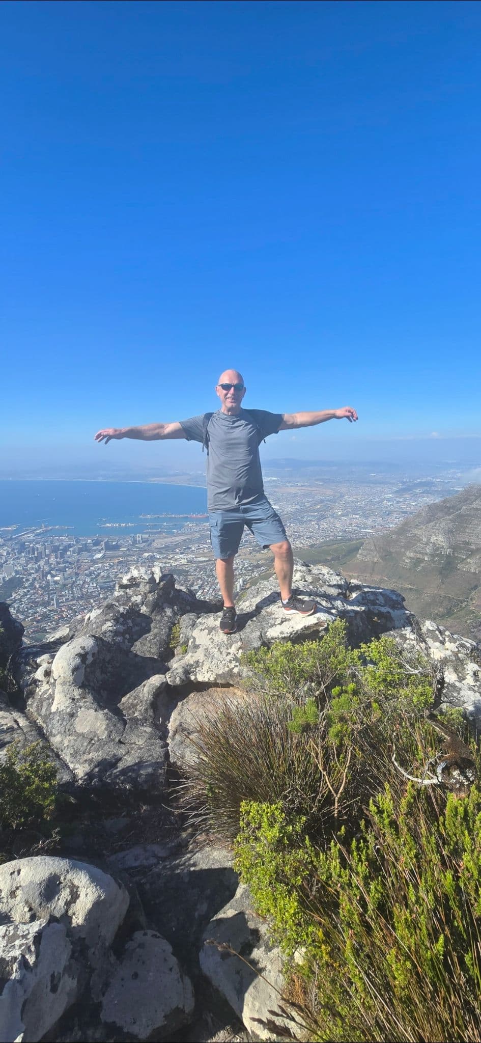 Table Mountain summit with a man standing with arms outstretched overlooking Cape Town, South Africa.