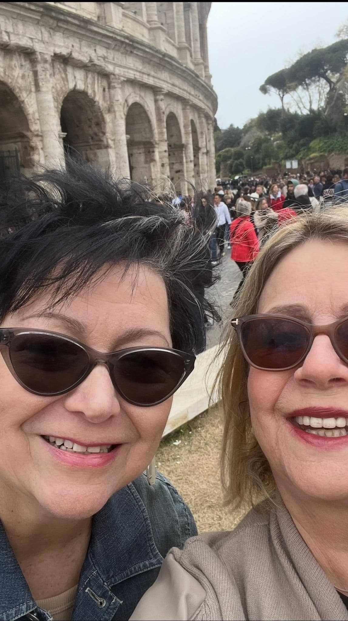 Colosseum in Rome, Italy with two women taking a selfie in front of the ancient amphitheater and a crowd behind them.