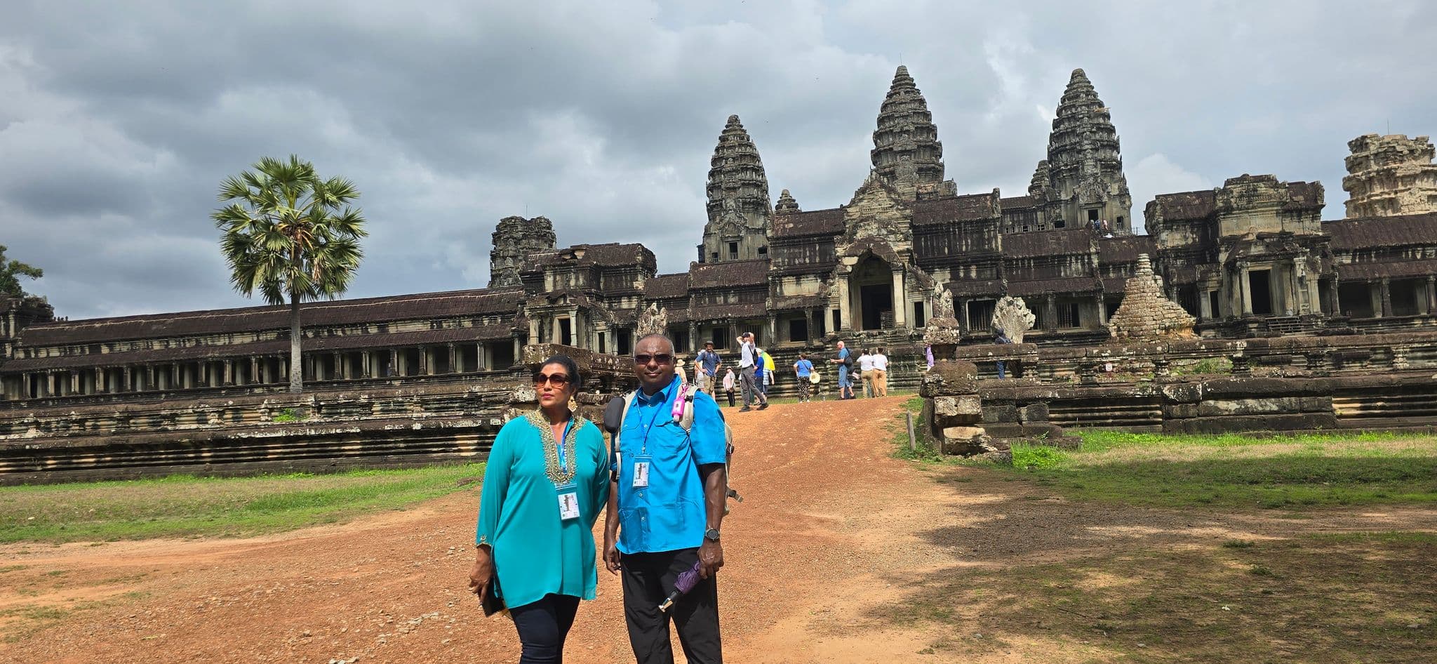 Angkor Wat temple complex in Siem Reap, Cambodia, with two travelers standing on the approach path in front of the central towers.
