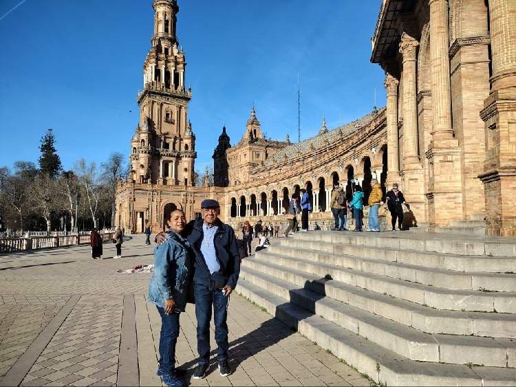 Plaza de España in Seville, Spain, with a couple posing on the plaza near the curved arcade and tower.