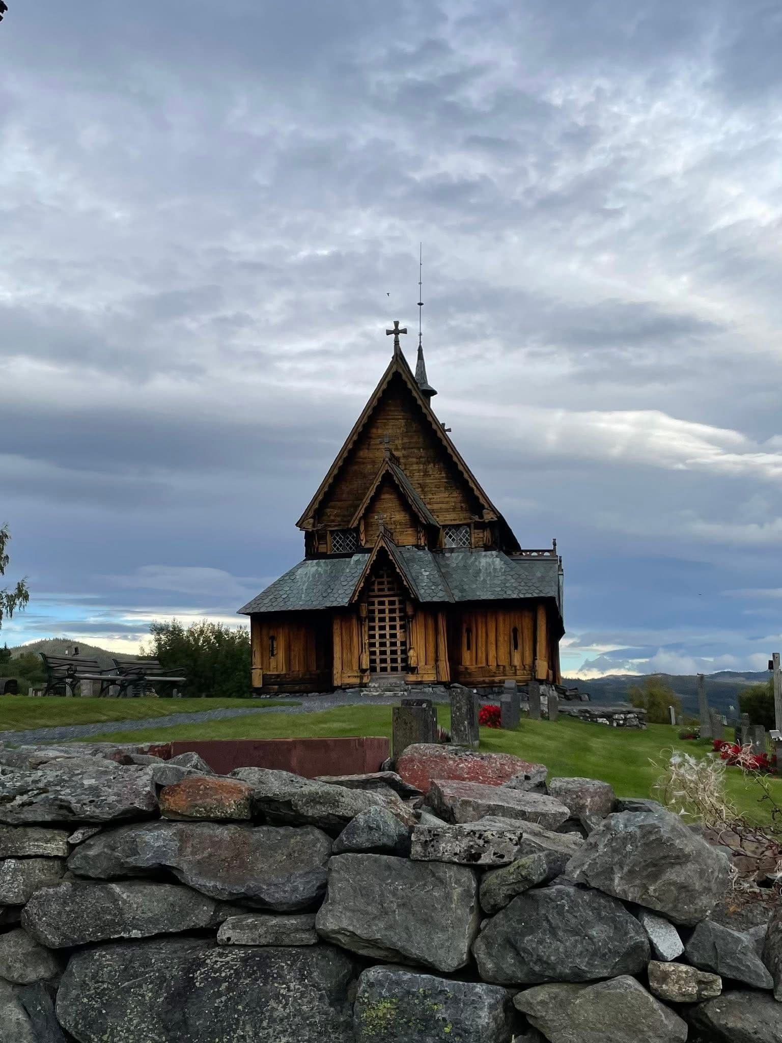 Heddal Stave Church behind a low stone wall under a cloudy sky in Notodden, Norway.