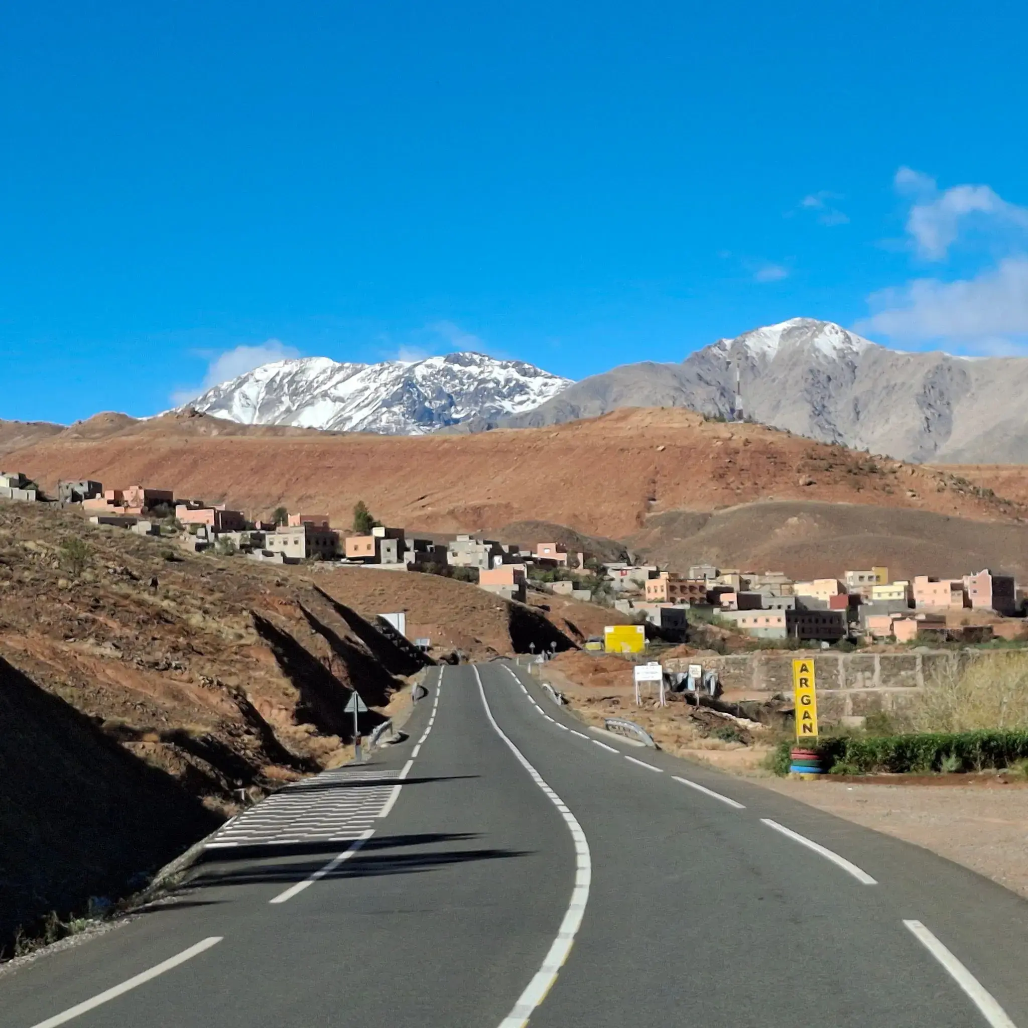 High Atlas Mountains rising behind a winding road and a hillside village in Morocco.