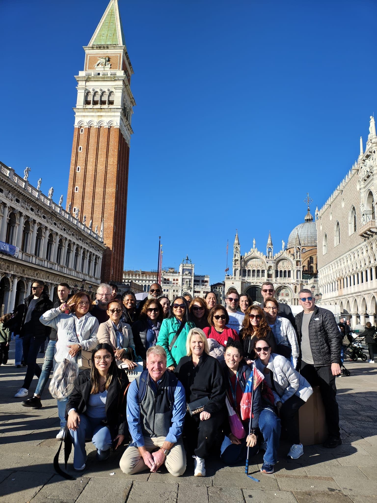 St Mark's Campanile and Basilica in Piazza San Marco, Venice, Italy, with a large tour group posing in the foreground.