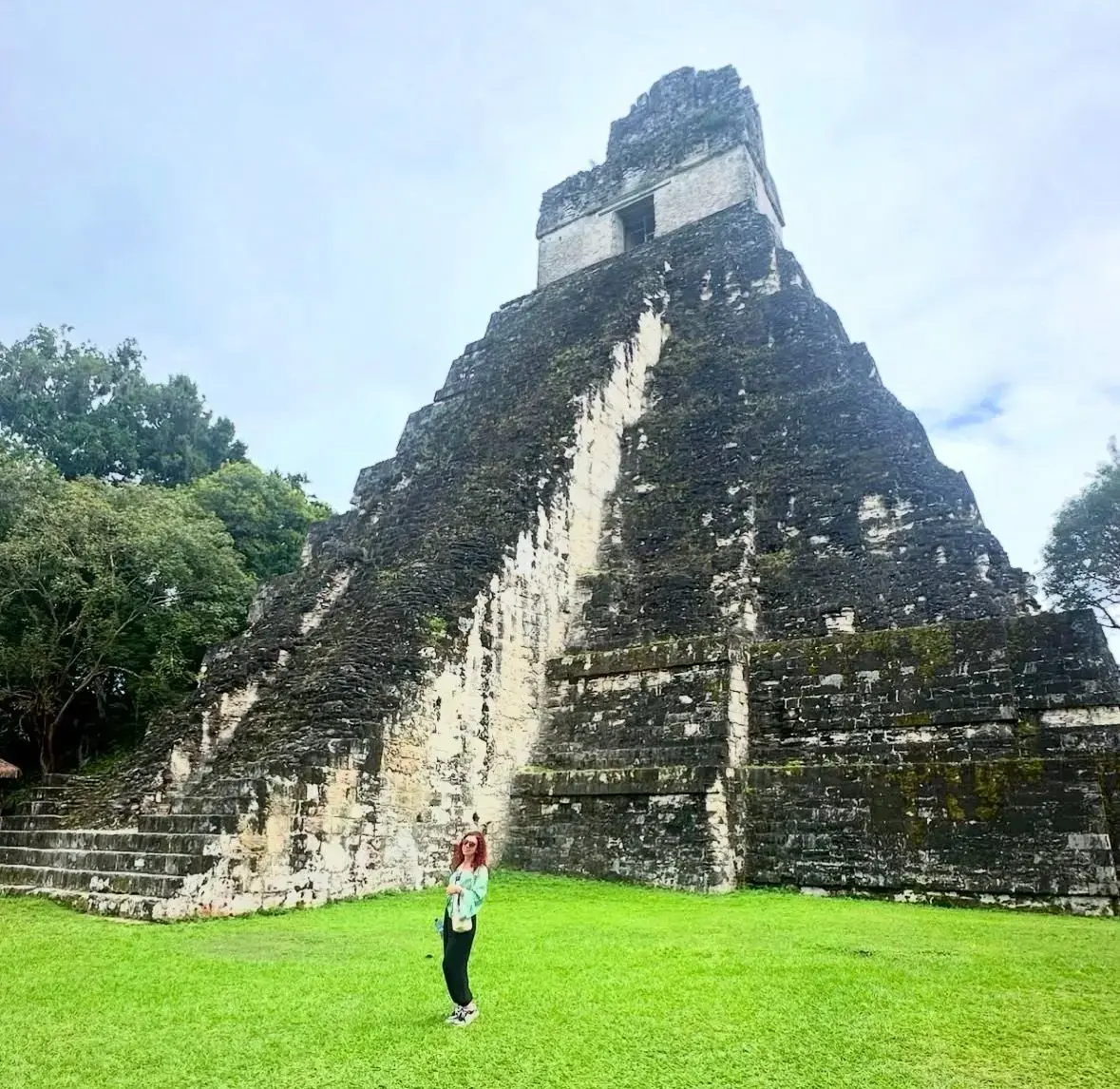 Temple I at Tikal, Guatemala with a traveler standing on the grassy foreground in front of the large stone pyramid.