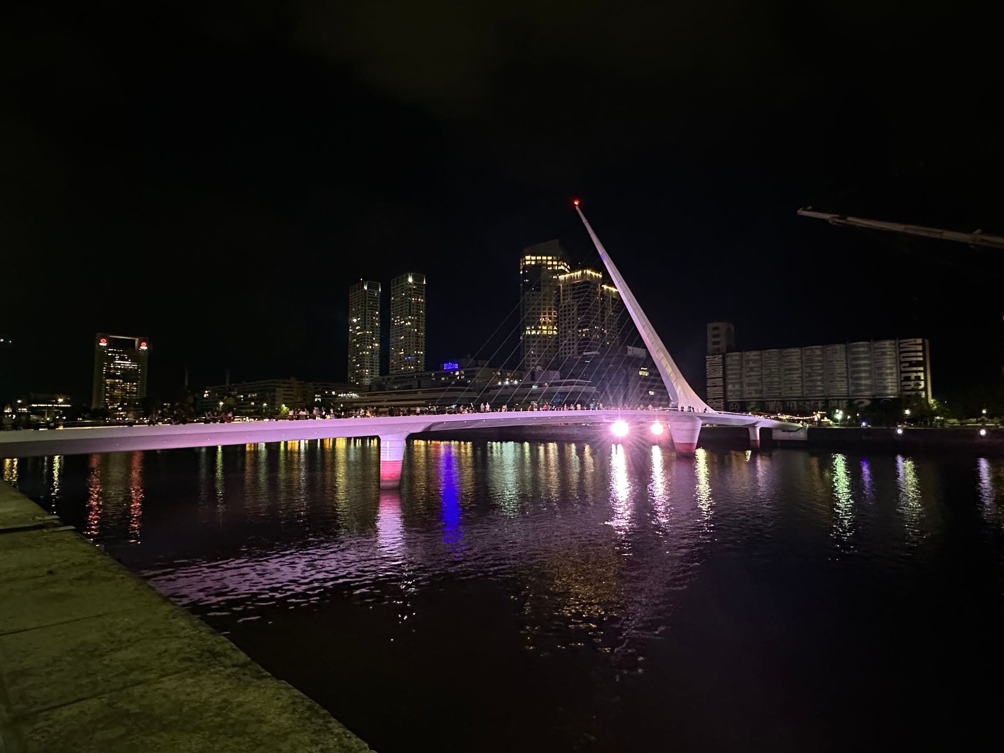 Puente de la Mujer lit at night, people walking across with lights reflecting in the water, Buenos Aires, Argentina.