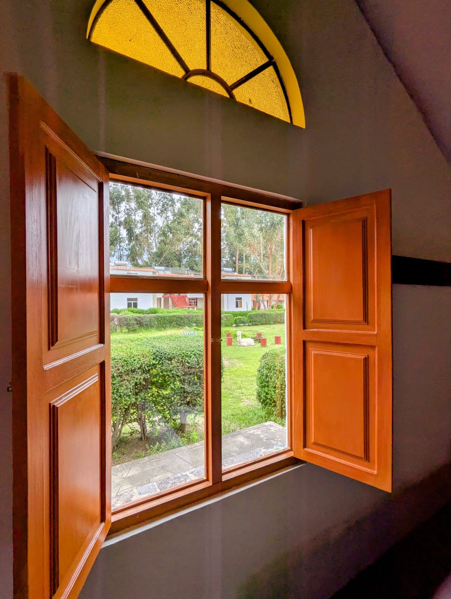 Open wooden window framing alpacas and hammocks in the garden of Casona Plaza Ecolodge, Colca Valley, Peru.