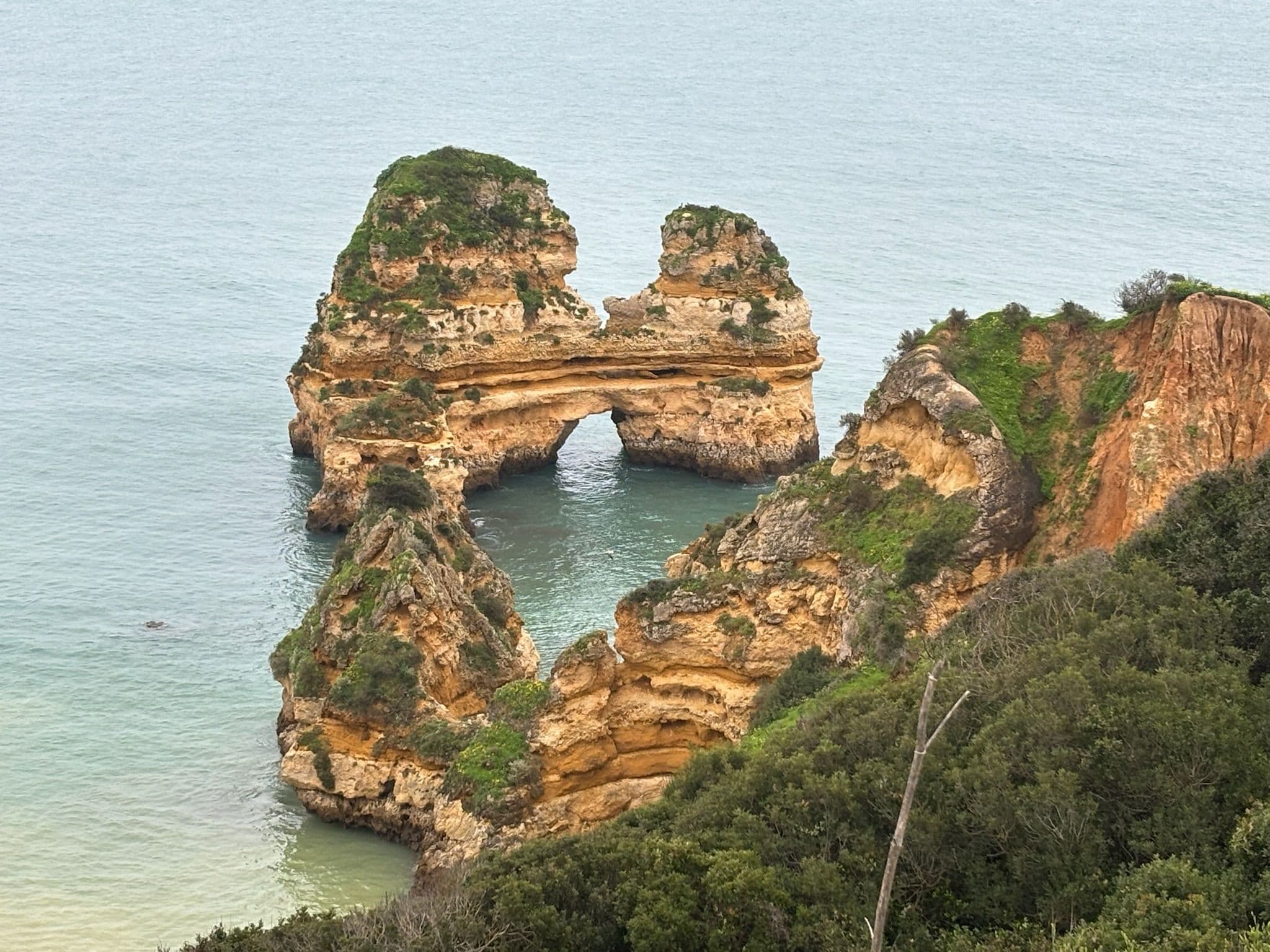 Limestone sea arch and rocky cliffs at Praia da Marinha on the Algarve coast, Portugal, viewed from a clifftop.