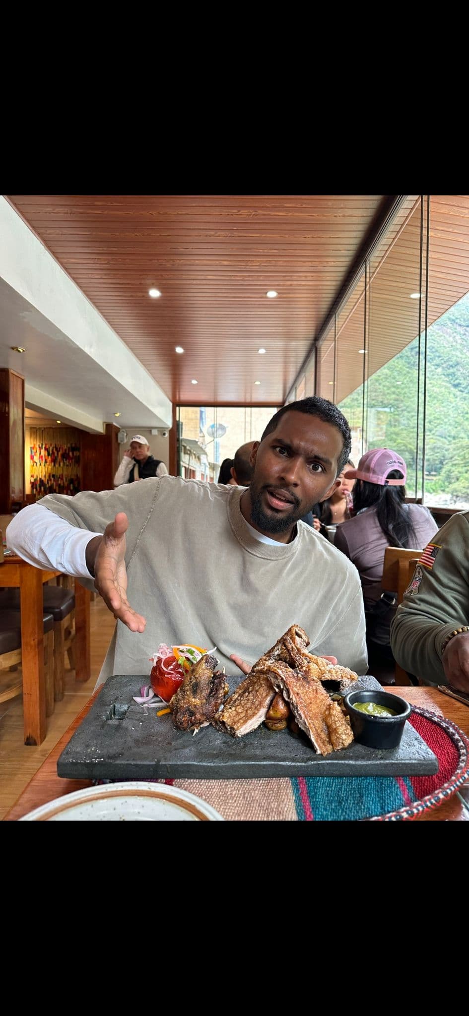 Roasted guinea pig on a stone platter with a man gesturing toward it inside a restaurant near Machu Picchu, Peru.