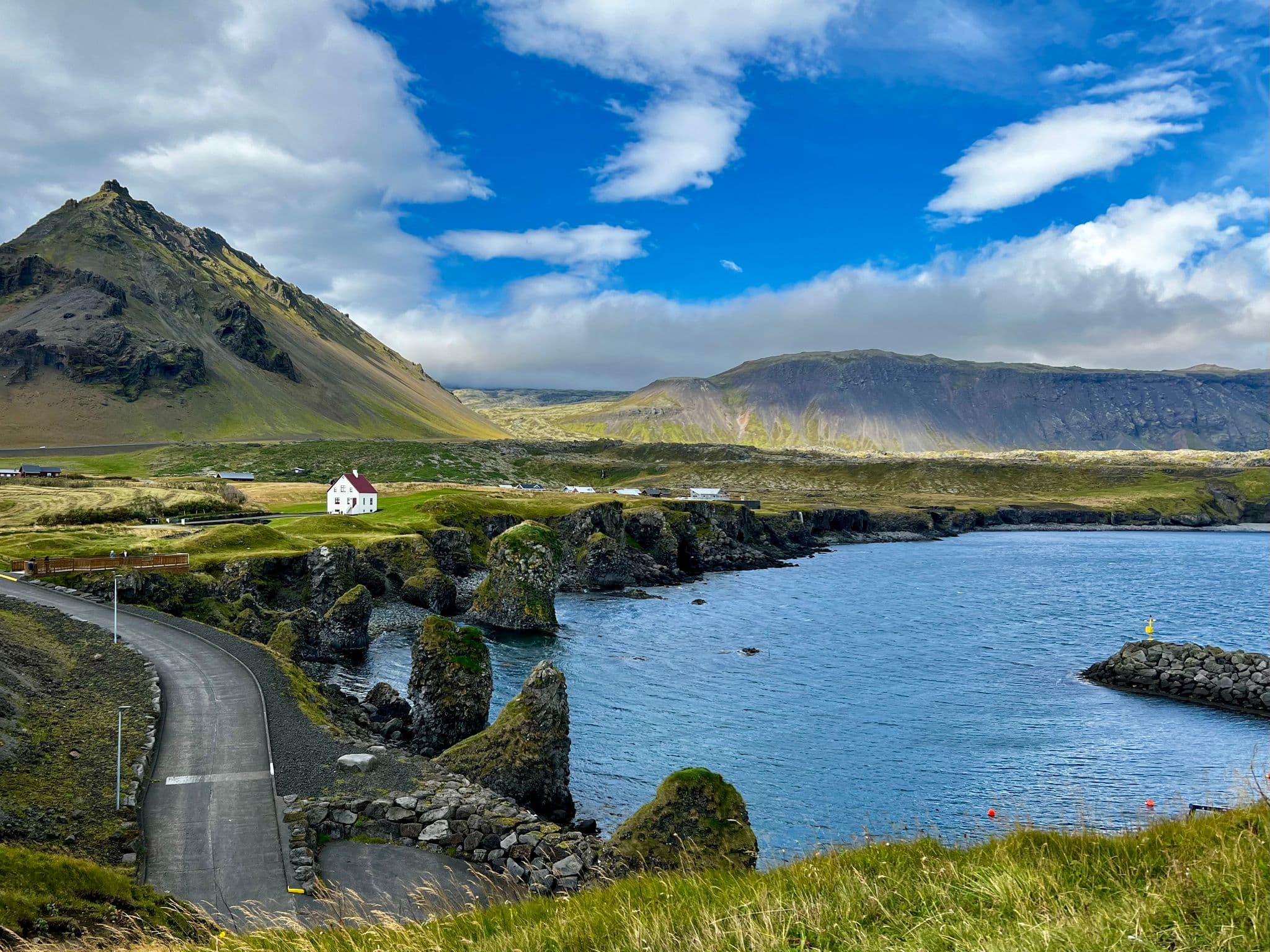 Rocky coastal sea stacks and a white house beside a winding road on the Snæfellsnes Peninsula, Iceland.