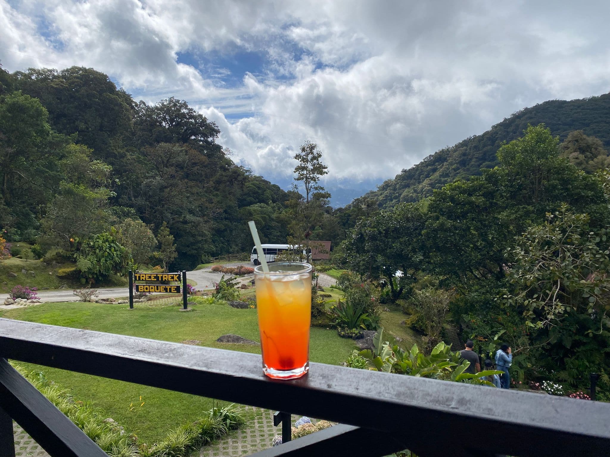 Cloud-forest hills at Tree Trek in Boquete, Panama, with a red-orange iced drink on a balcony railing in the foreground.