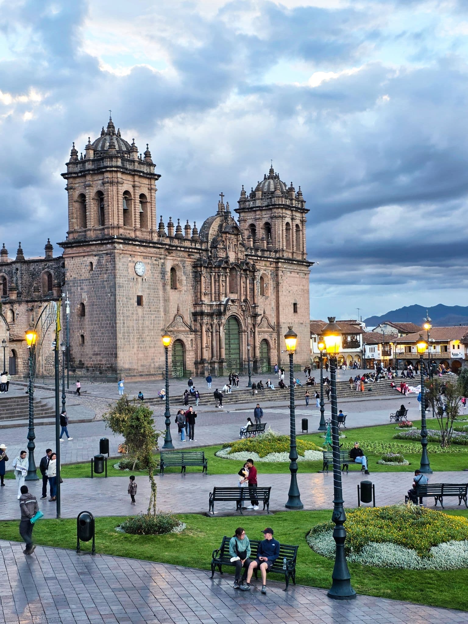 Cusco Cathedral on the Plaza de Armas with people strolling, sitting on benches, and city lights in Cusco, Peru