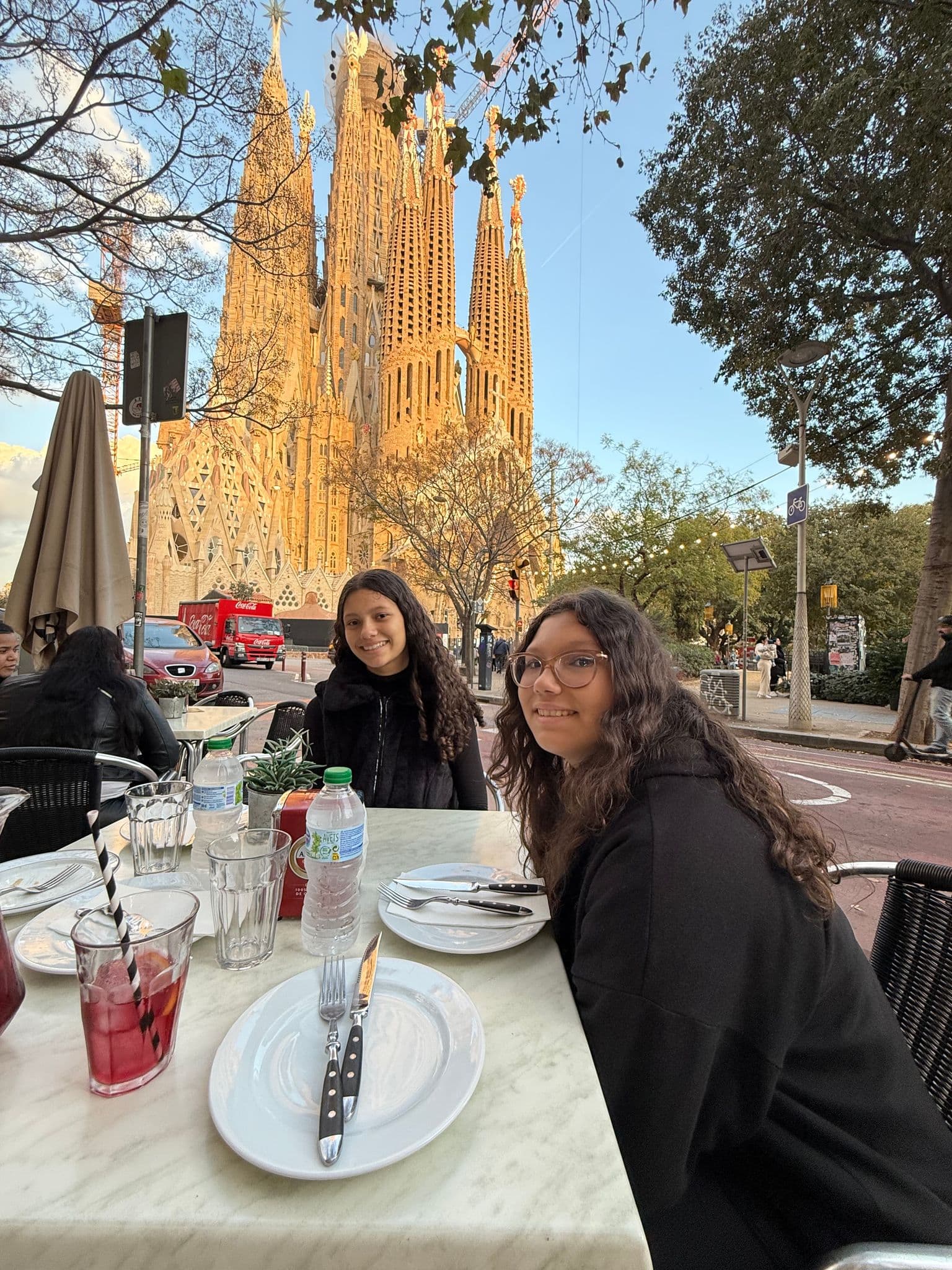 Sagrada Família in Barcelona seen behind two people seated at an outdoor dinner table at sunset, Spain.