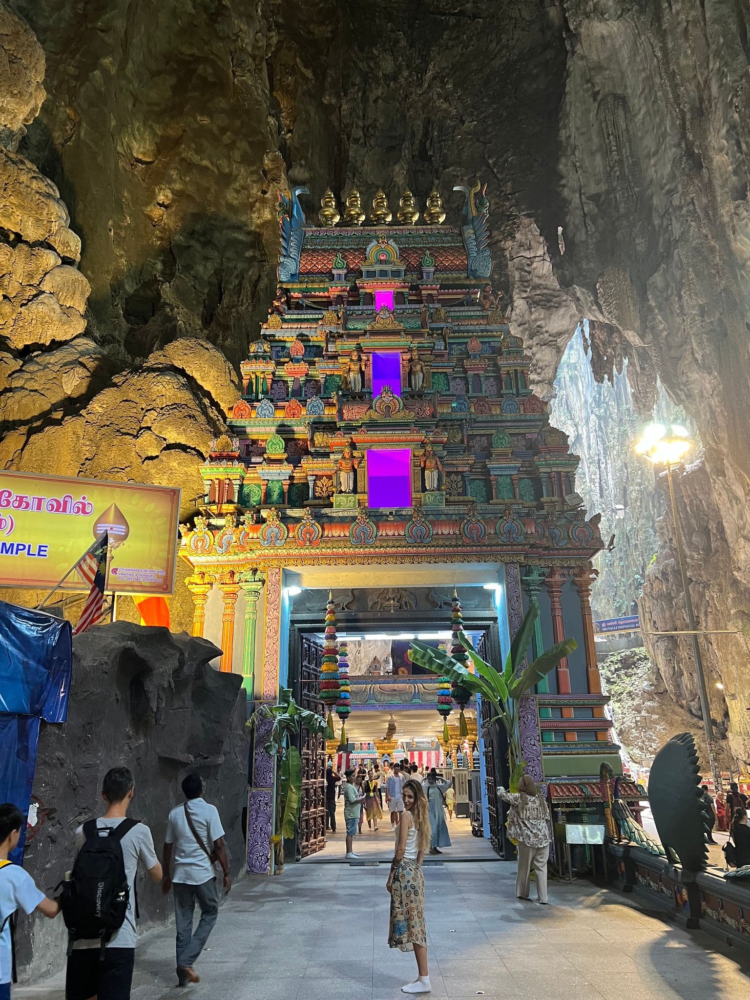 Batu Caves temple gateway (gopuram) inside a limestone cave in Kuala Lumpur, Malaysia, with visitors and a woman looking back.