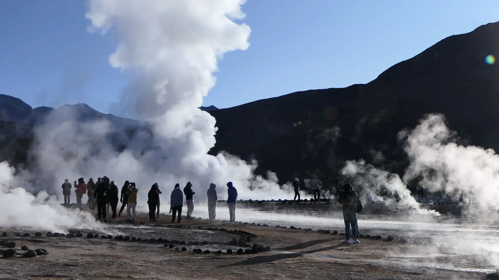 Steam plumes rising from geothermal geysers as tourists photograph the scene at El Tatio Geysers, Chile.