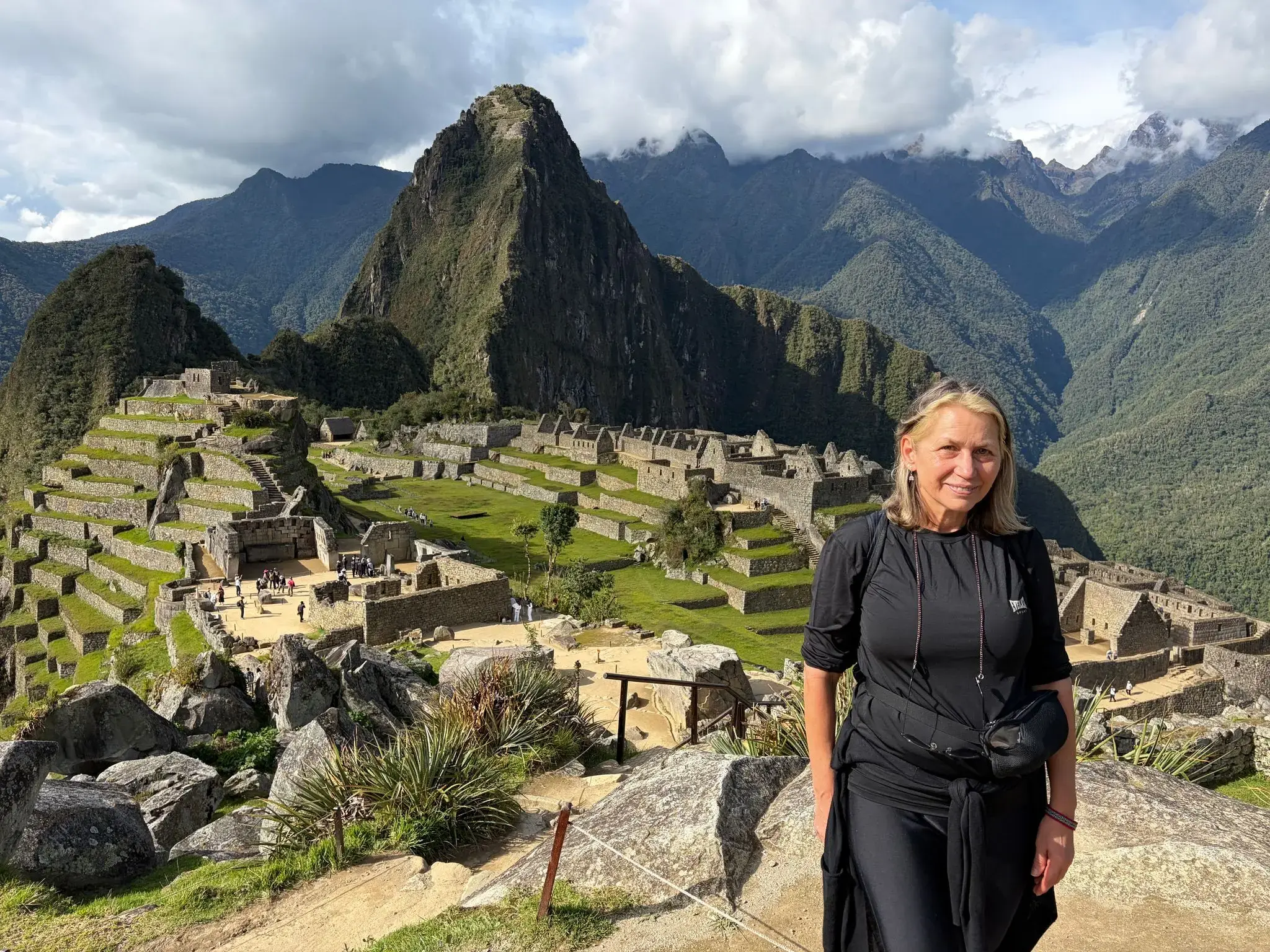 Machu Picchu ruins with terraces and Huayna Picchu peak in the background, a traveler standing in the foreground, Cusco region, Peru.