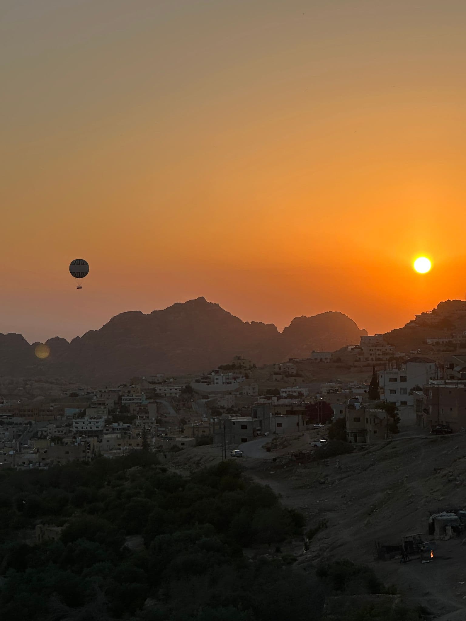 Hot air balloon floating over Petra's rocky cliffs at sunset, with the town below, Jordan