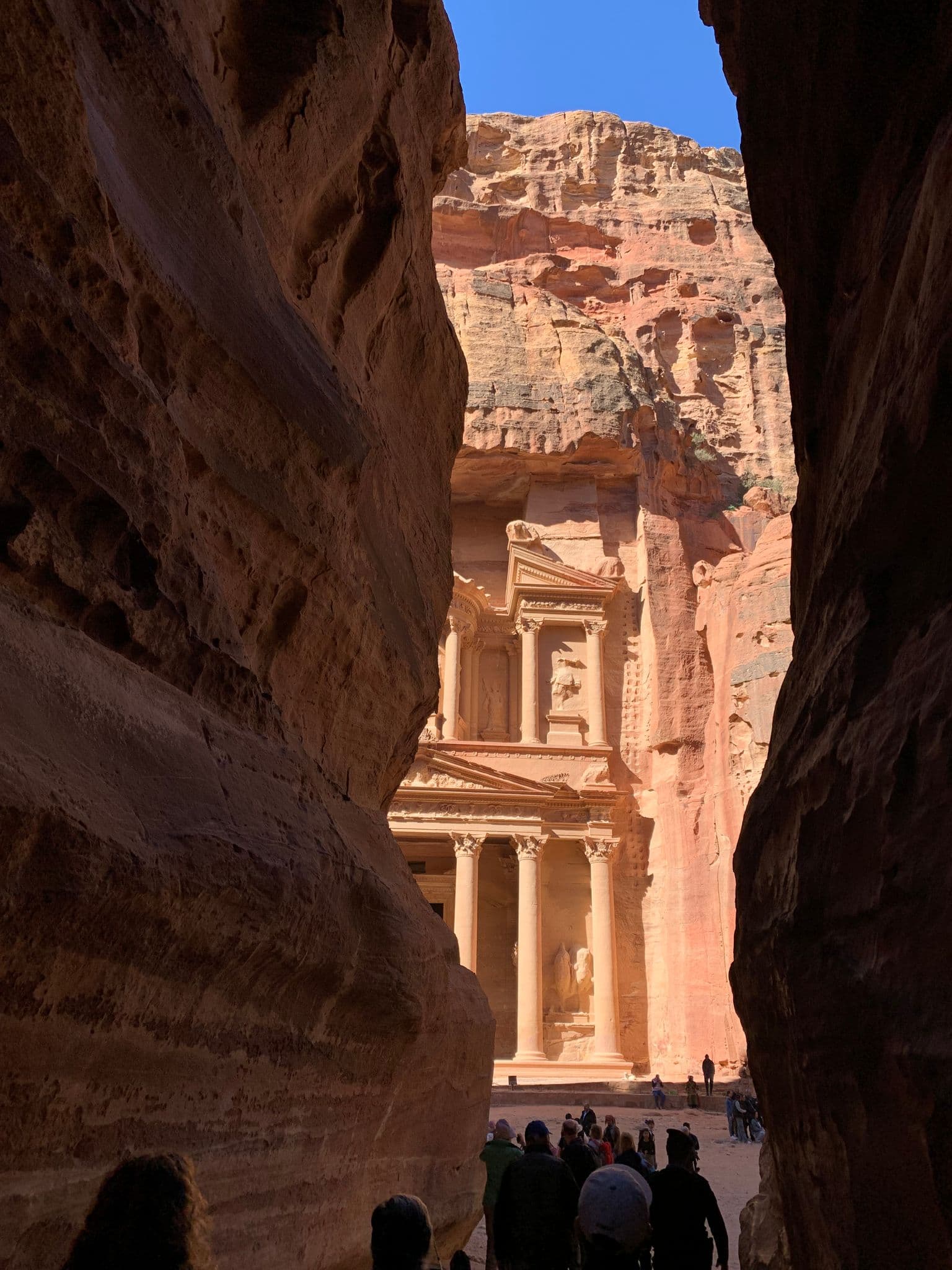 Al-Khazneh (the Treasury) at Petra seen through the narrow siq with tourists walking toward the carved façade, Petra, Jordan.
