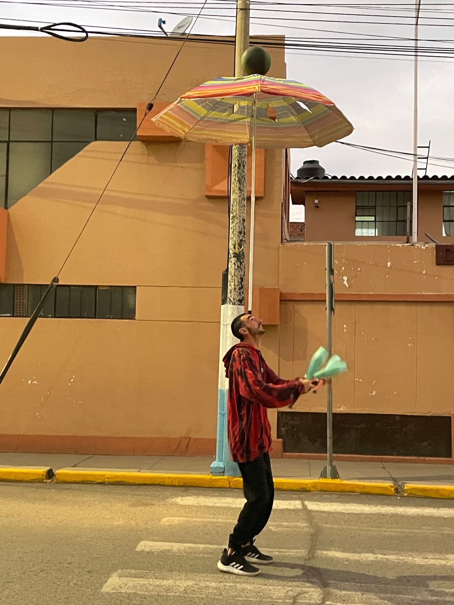 Street performer juggling clubs beneath a striped umbrella on a sidewalk in Puno, Peru.