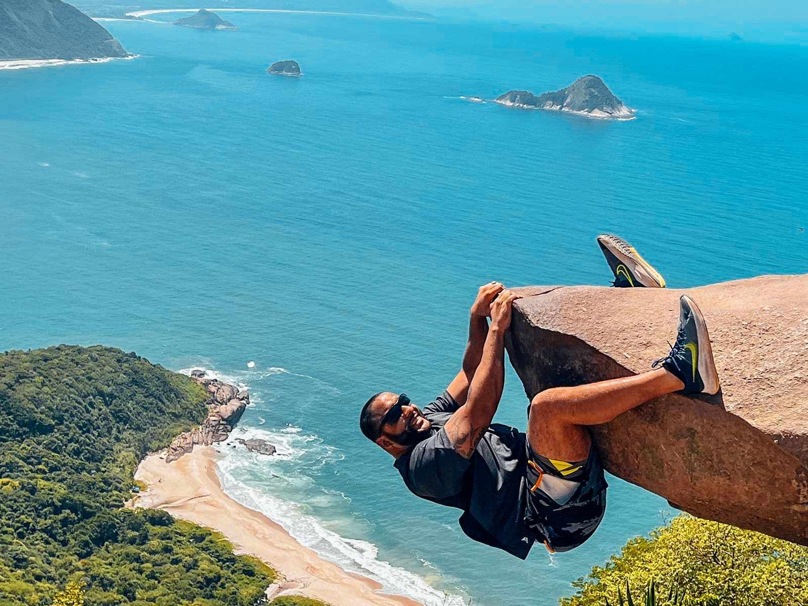 Pedra do Telégrafo rock with a person hanging from its edge above the ocean near Rio de Janeiro, Brazil.