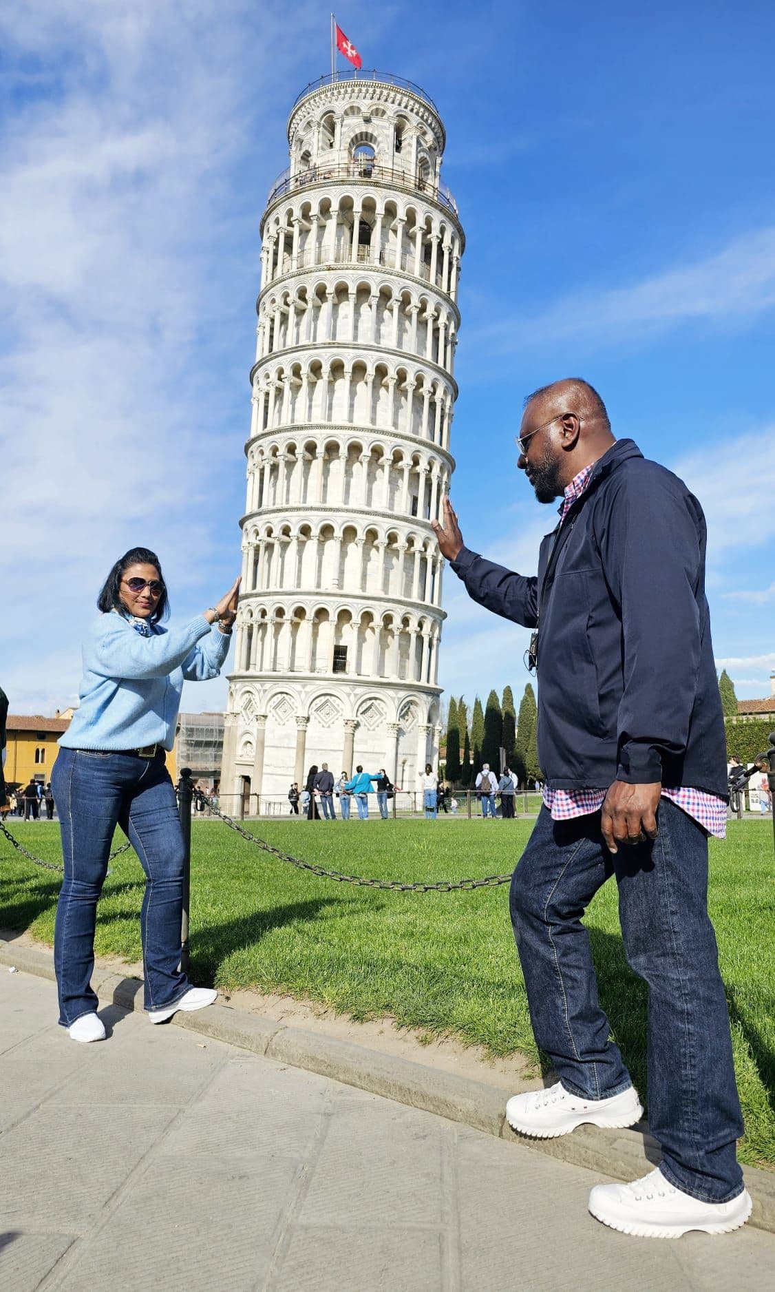 Leaning Tower of Pisa with two travelers posing as if holding the tower at Piazza dei Miracoli, Pisa, Italy.