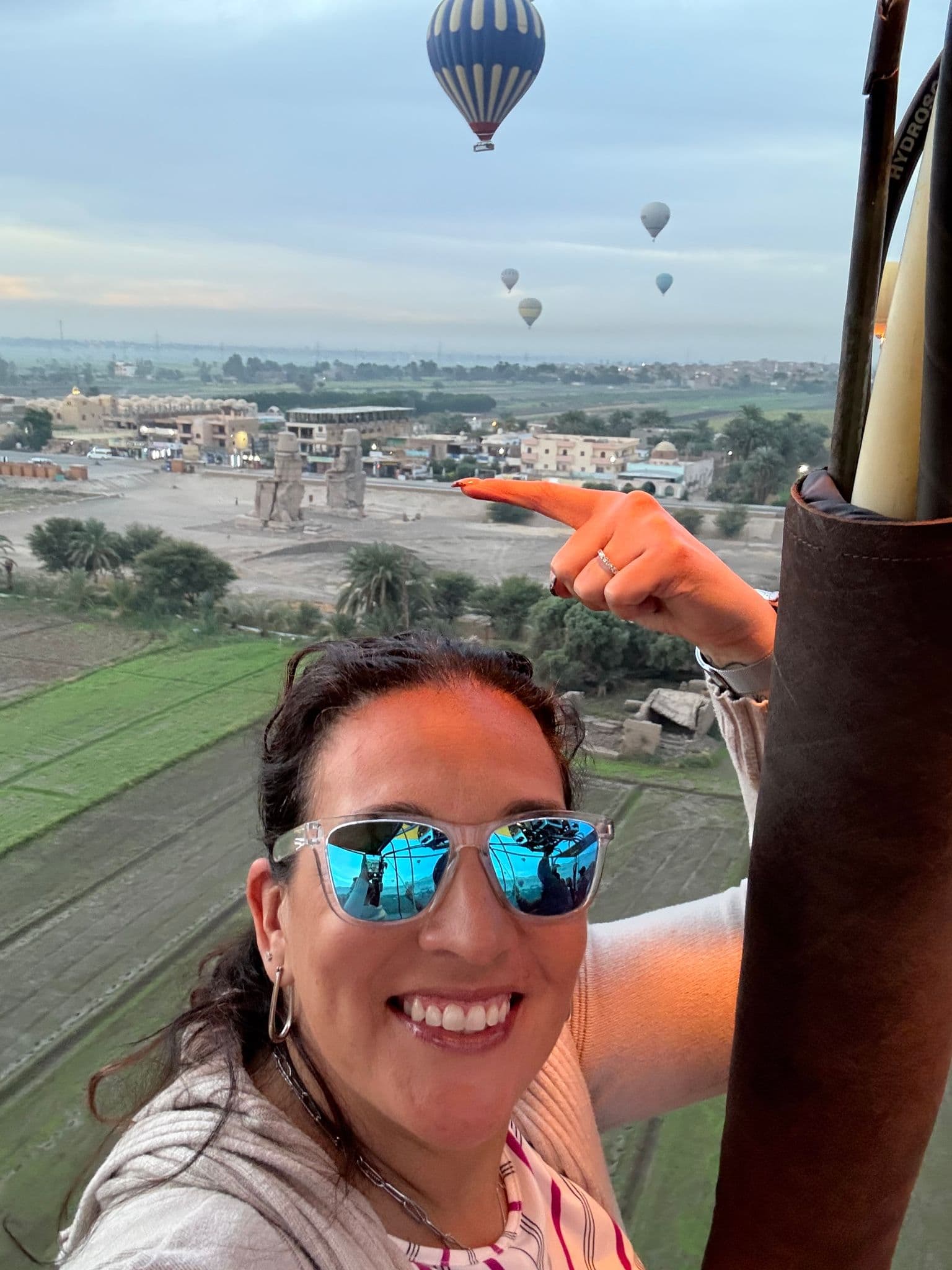 Colossi of Memnon with hot air balloons overhead and a woman taking a selfie from a hot air balloon, Luxor, Egypt.