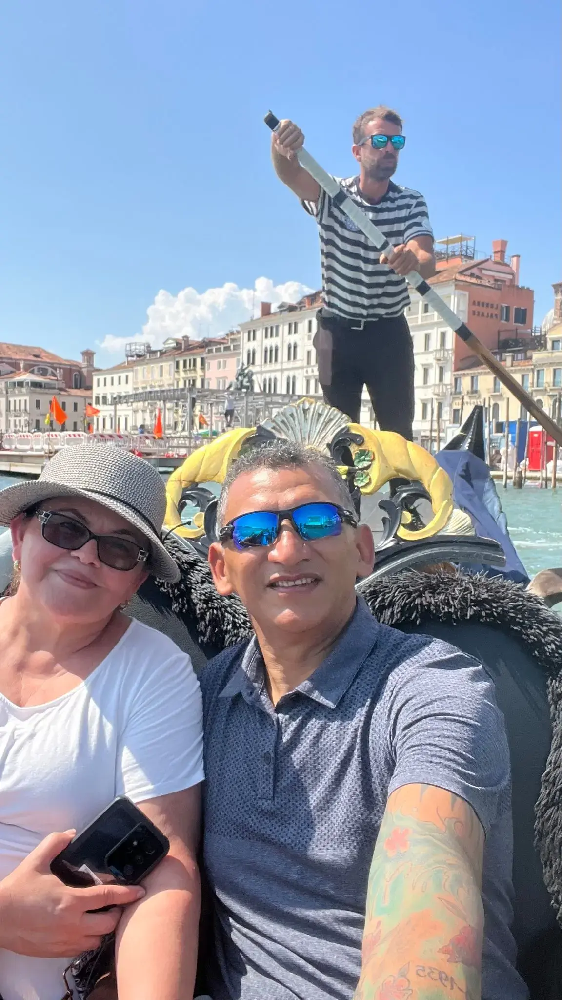 Gondola on the Grand Canal in Venice, Italy, with a couple taking a selfie and a gondolier steering behind them.