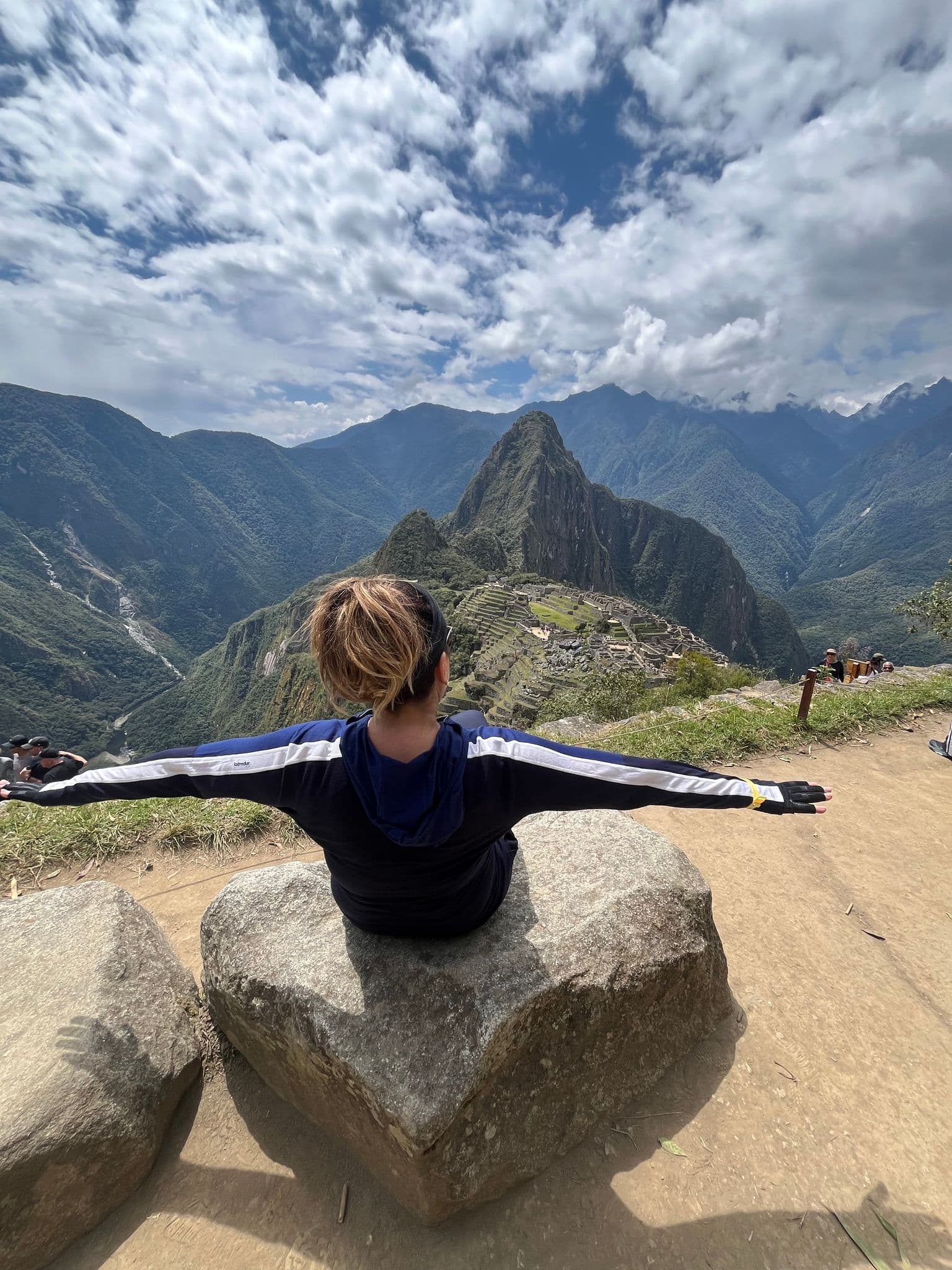Machu Picchu ruins with a traveler sitting on a rock, arms outstretched, overlooking the site near Cusco, Peru.
