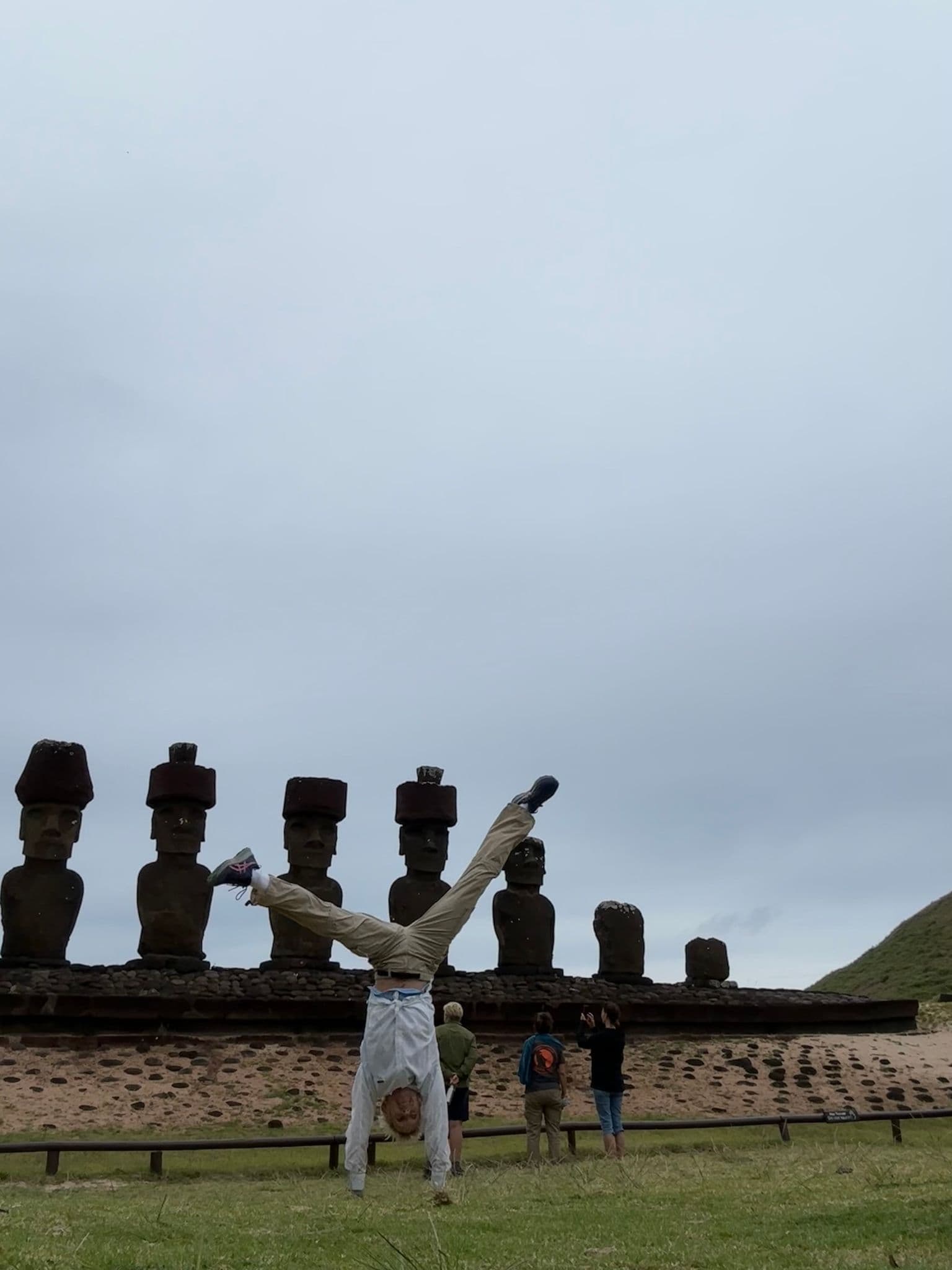 Ahu Tongariki moai on Easter Island with a person doing a cartwheel in front while other visitors photograph the site, Chile.