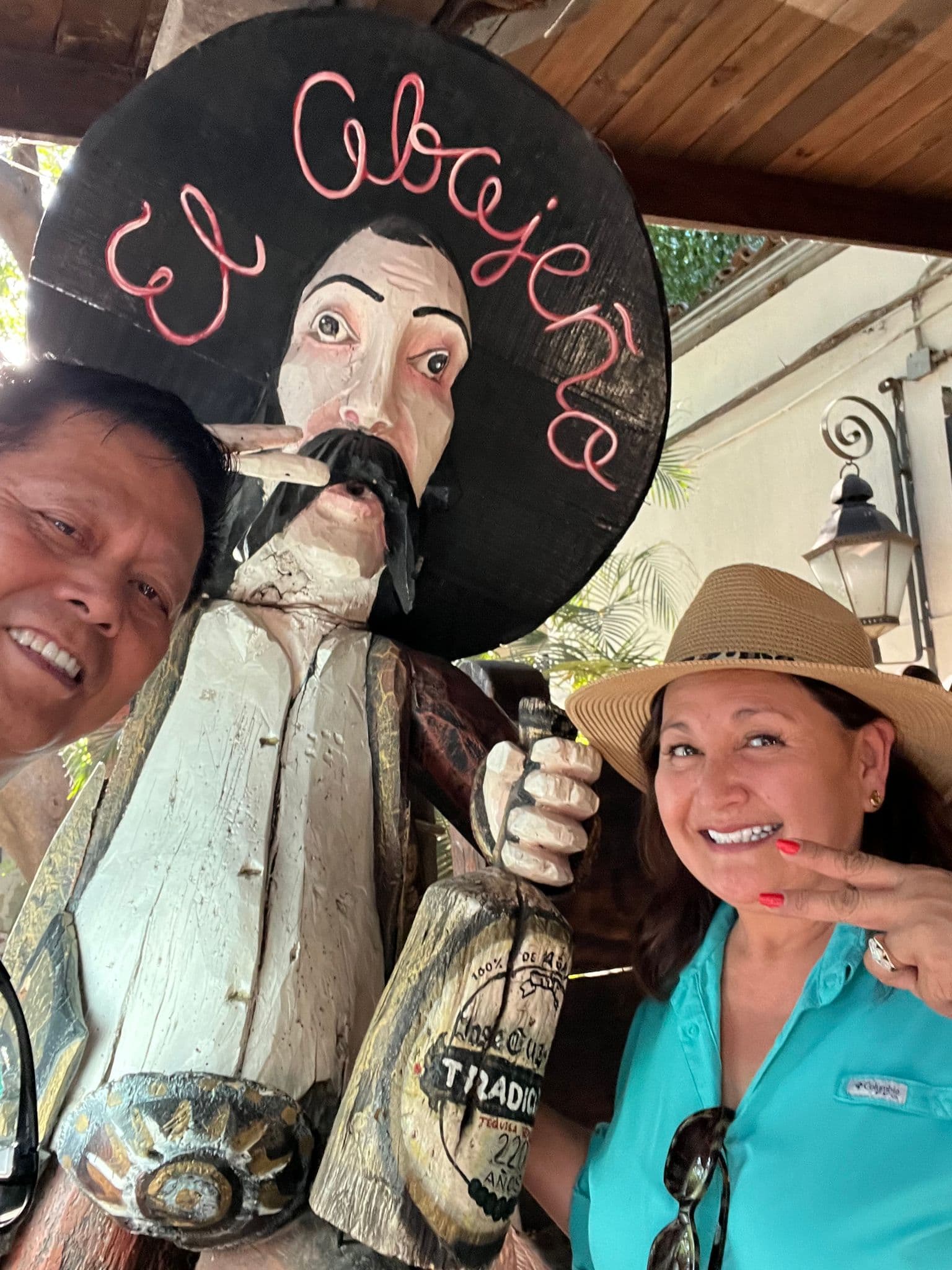 Wooden sombrero-wearing statue with two travelers smiling and posing for a selfie on a Colonial Mexico tour, Mexico.