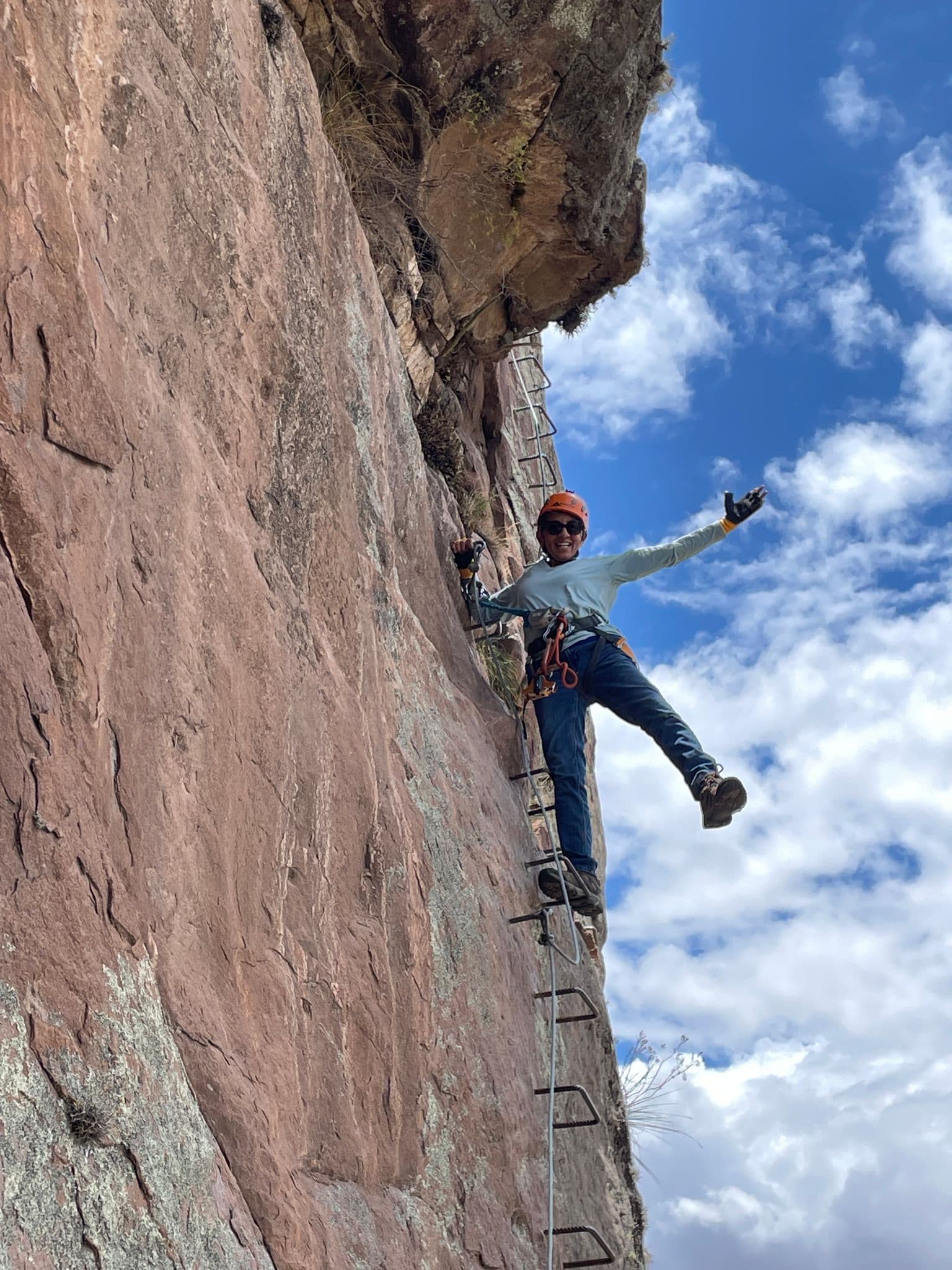 Climber on a via ferrata ladder standing on metal rungs on a steep red rock face near Cuzco, Peru.