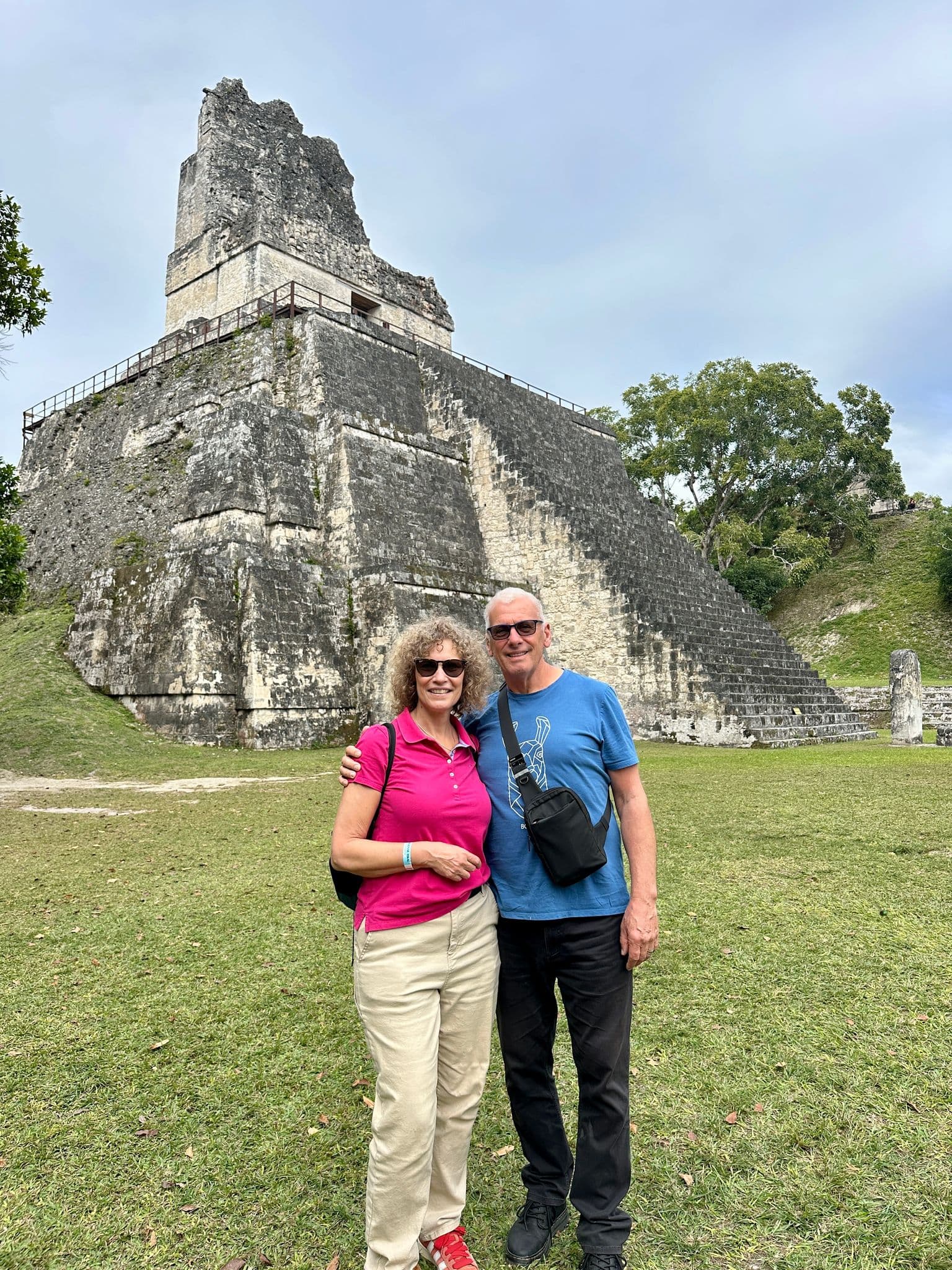 Temple I at Tikal, a stepped Maya pyramid, with a couple standing and posing on the grassy plaza, Tikal, Petén, Guatemala.